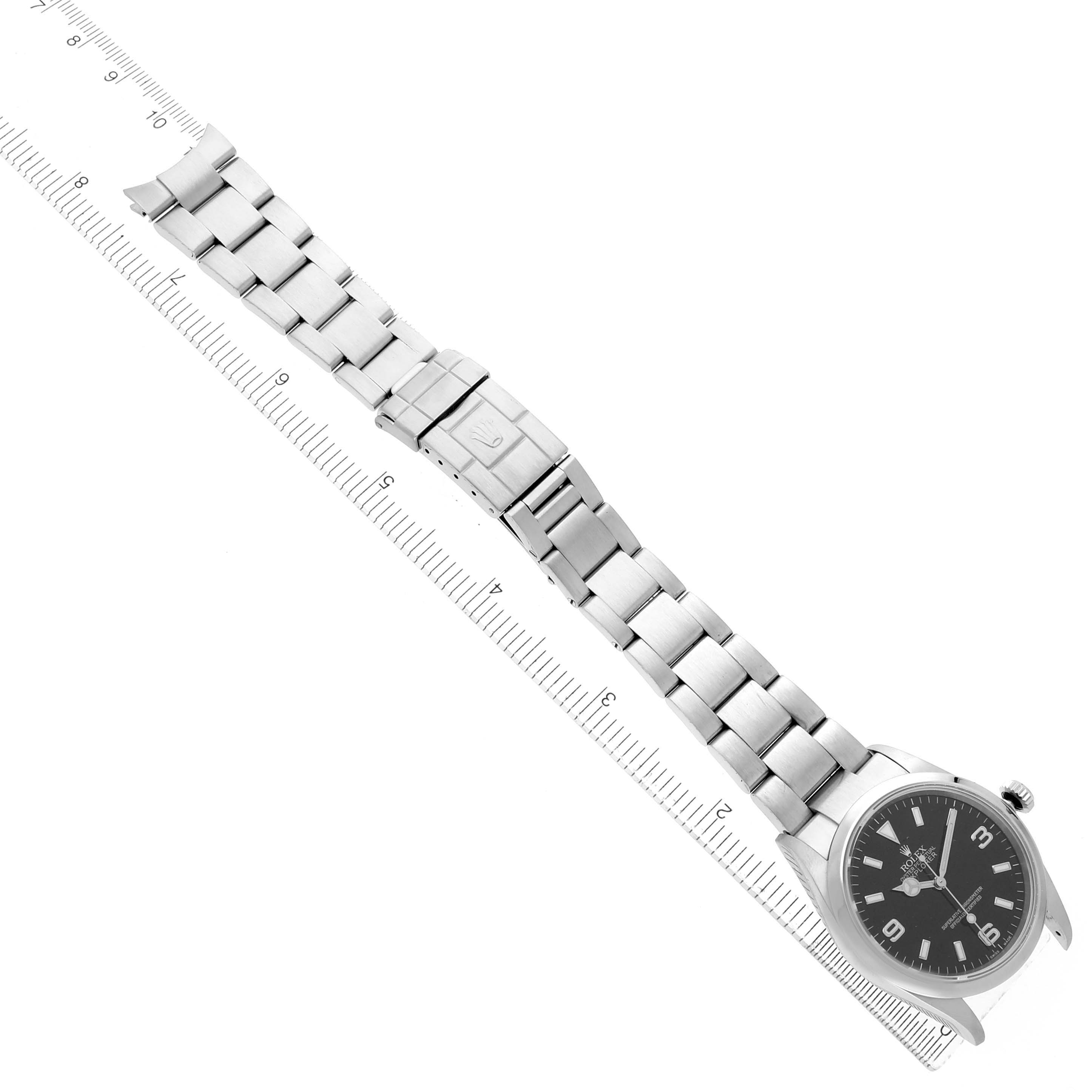 The Rolex Explorer 114270 Men's Stainless Steel Black Dial watch is shown from an overhead angle, highlighting the face, bracelet, and clasp alongside a measuring scale.