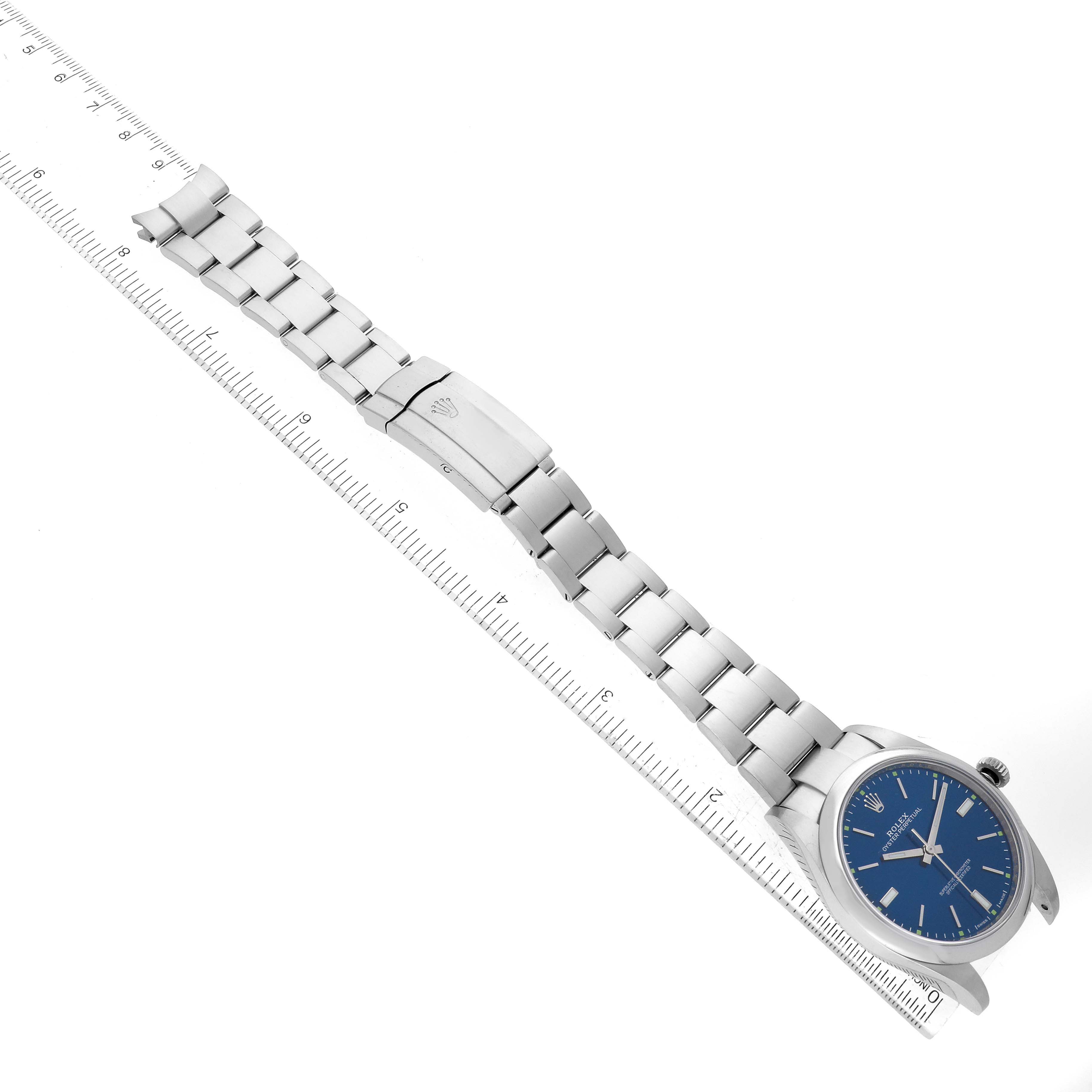 This image shows a top-down view of a Rolex Oyster Perpetual 114300 Men's Stainless Steel Blue Dial 114300 Men's Stainless Steel Blue Dial watch with a ruler beside it for scale.