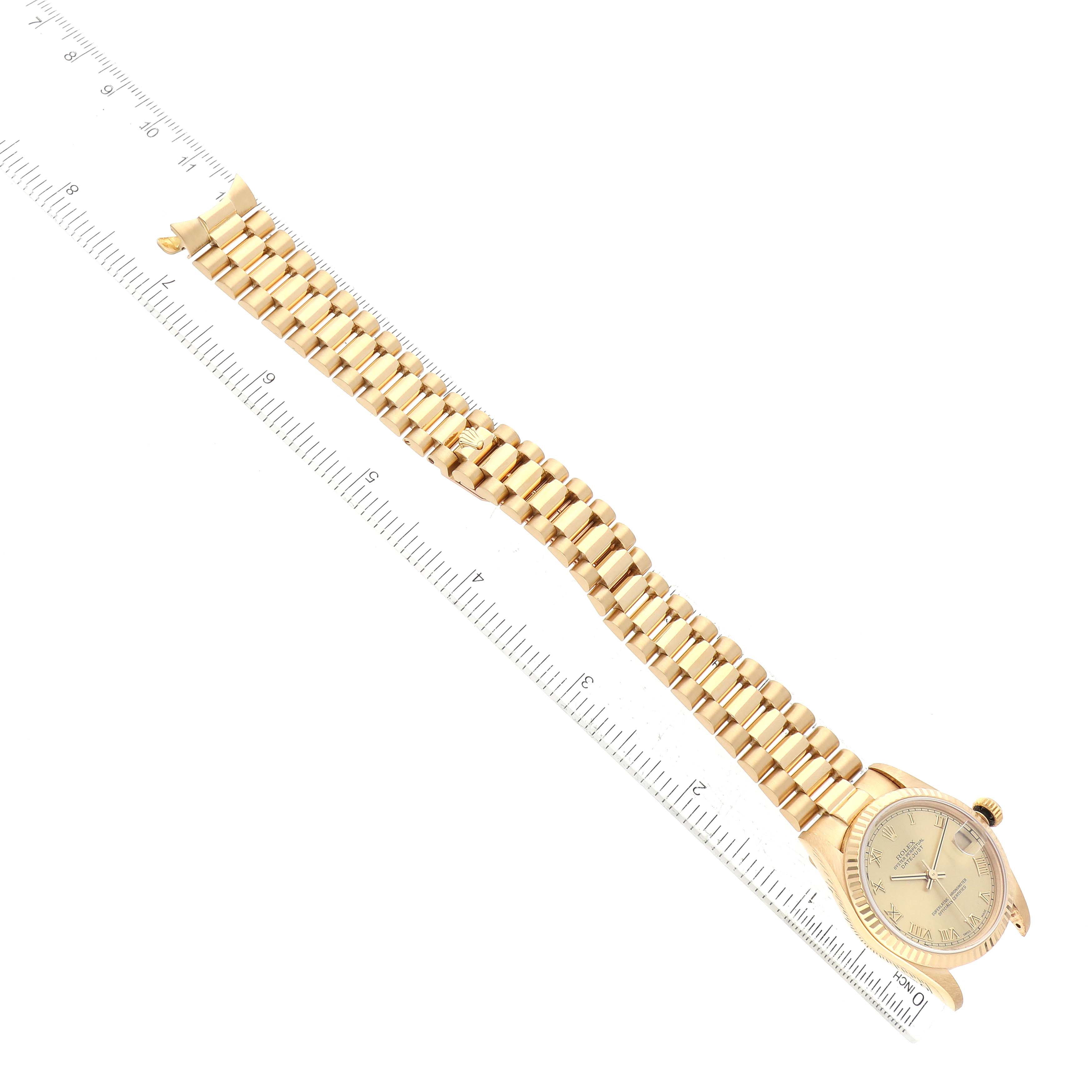 The image shows a Rolex President 68278 Women
s Yellow Gold Champagne Dial 68278 Women
s Yellow Gold Champagne Dial model watch laid flat, highlighting its gold bracelet and face with a ruler for scale reference.