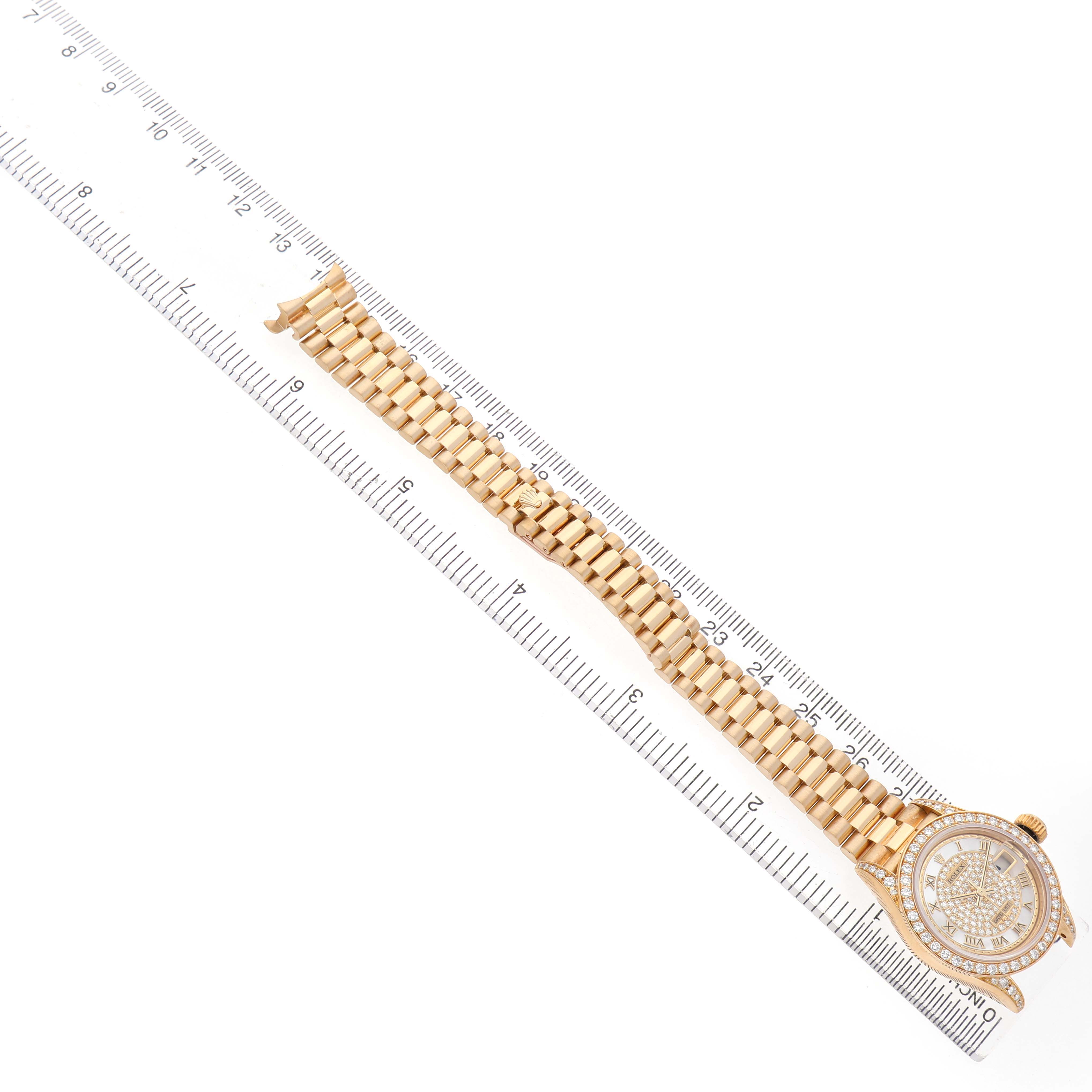 The image shows a Rolex President 69158 Women's Yellow Gold Mother of Pearl Dial watch laid flat on a ruler, highlighting its bracelet and face from a top-down angle.