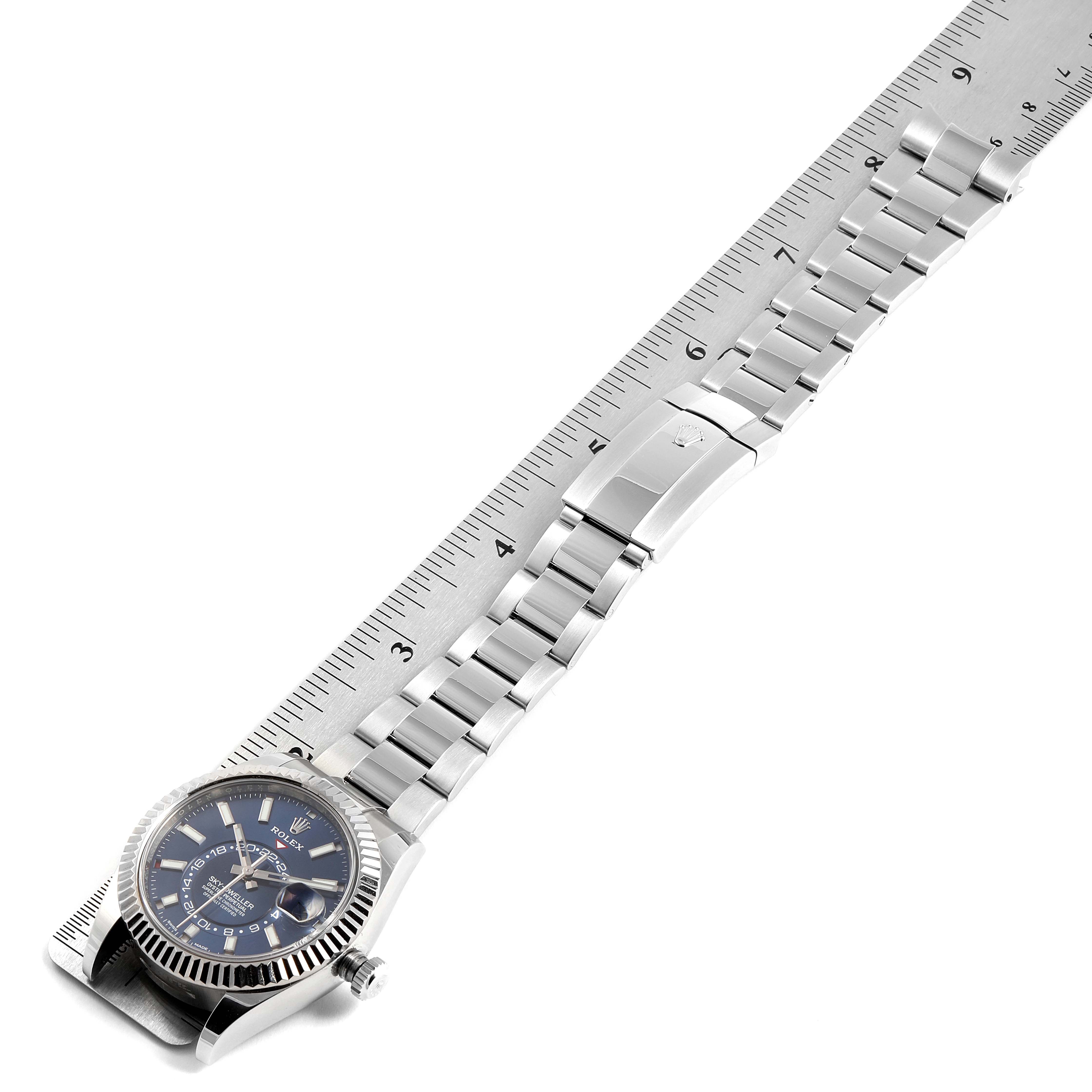 The Rolex Sky-Dweller 326934 Men's Stainless Steel Blue Dial 326934 Men's Stainless Steel Blue Dial watch is shown from a top-down angle, including its face, bracelet, and clasp, set alongside a ruler.