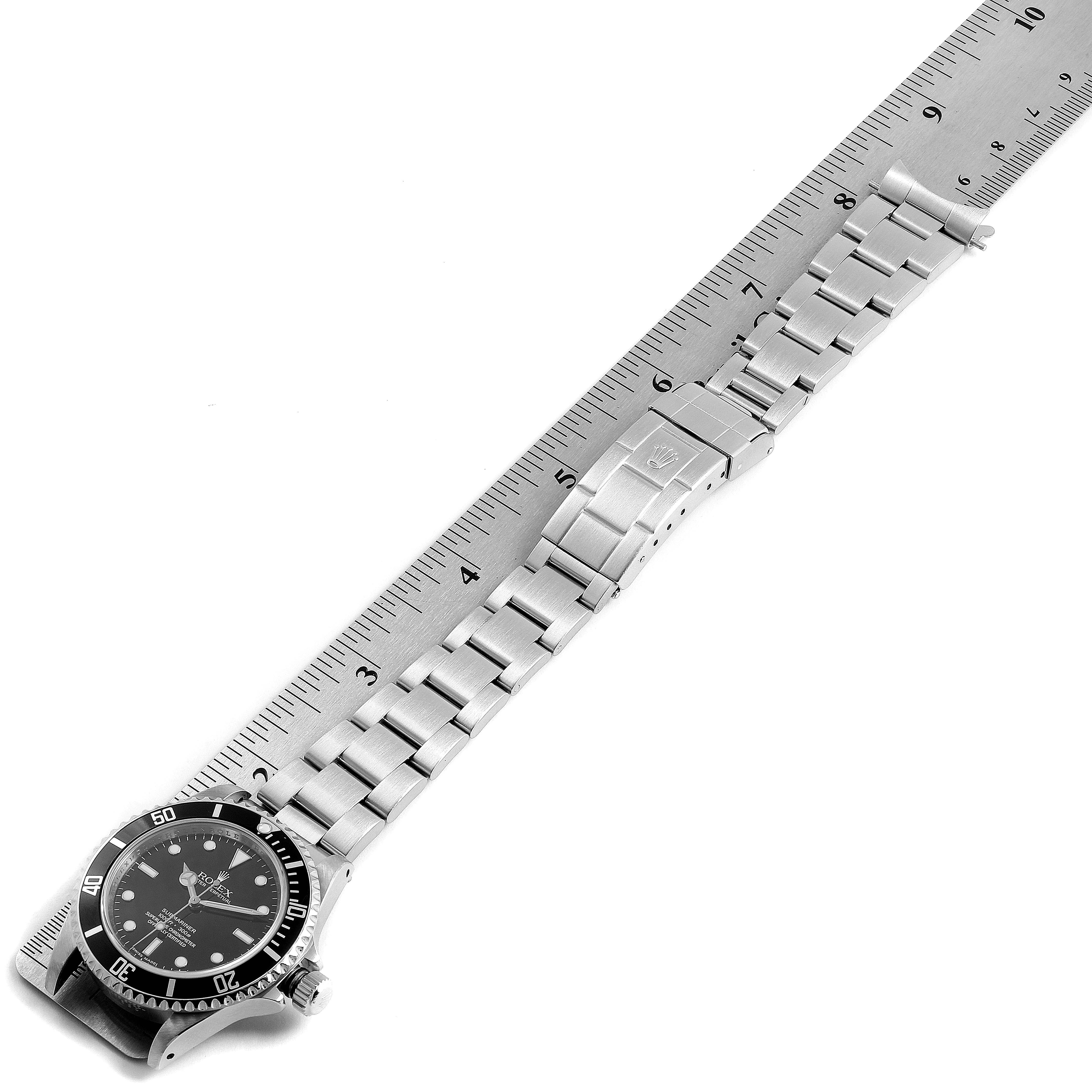 The Rolex Submariner 14060M Men's Stainless Steel Black Dial 14060M Men's Stainless Steel Black Dial watch is shown from a diagonal top-down angle, alongside a ruler for scale measurement of the bracelet.