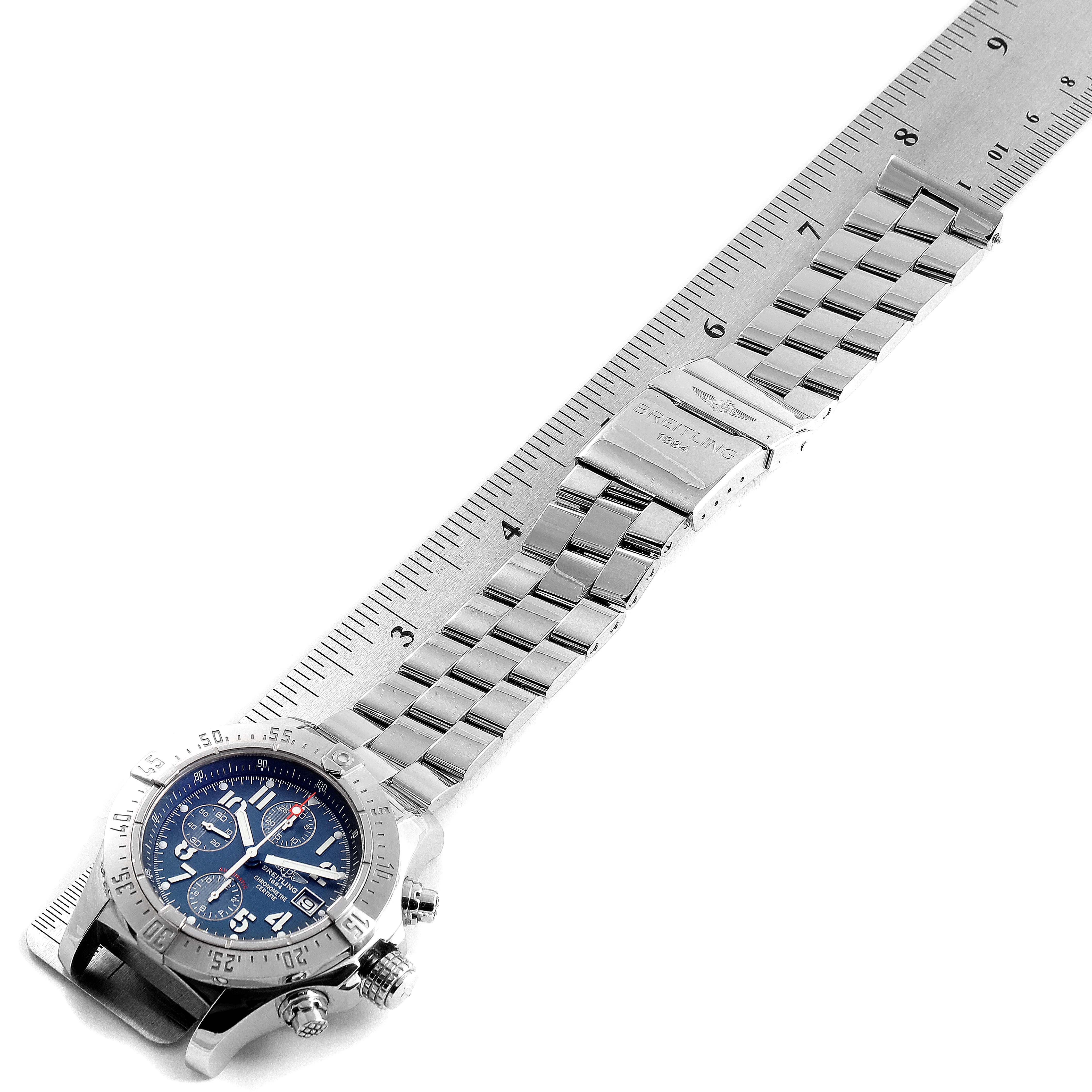 The image shows a Breitling Avenger A13381 Men's Stainless Steel Blue Dial A13381 Men's Stainless Steel Blue Dial watch laying face-up with its stainless steel bracelet extended next to a ruler.