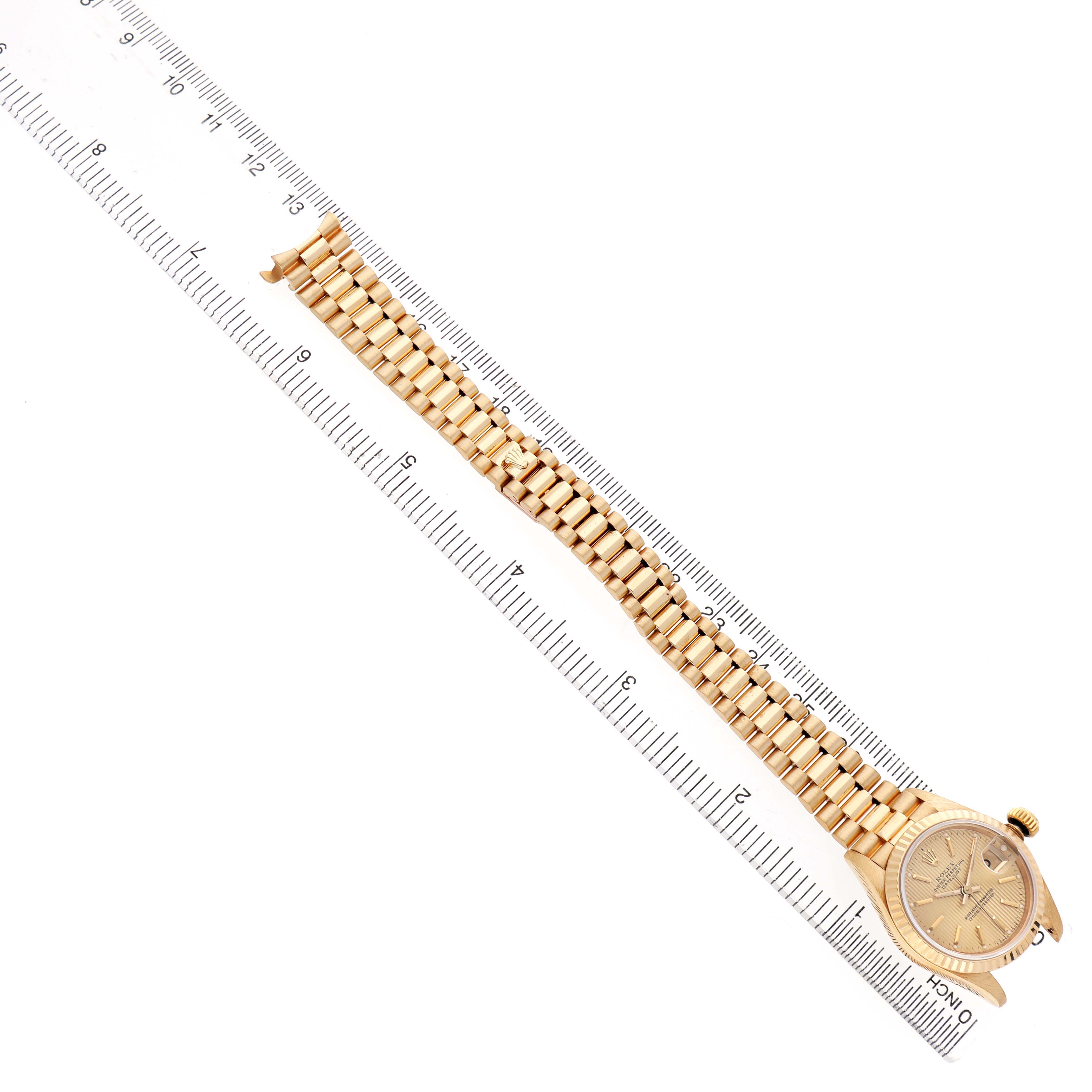The Rolex President 69178 Women's Yellow Gold Champagne Dial model watch is shown from a top-down angle, displaying the entire band and watch face placed along a ruler.
