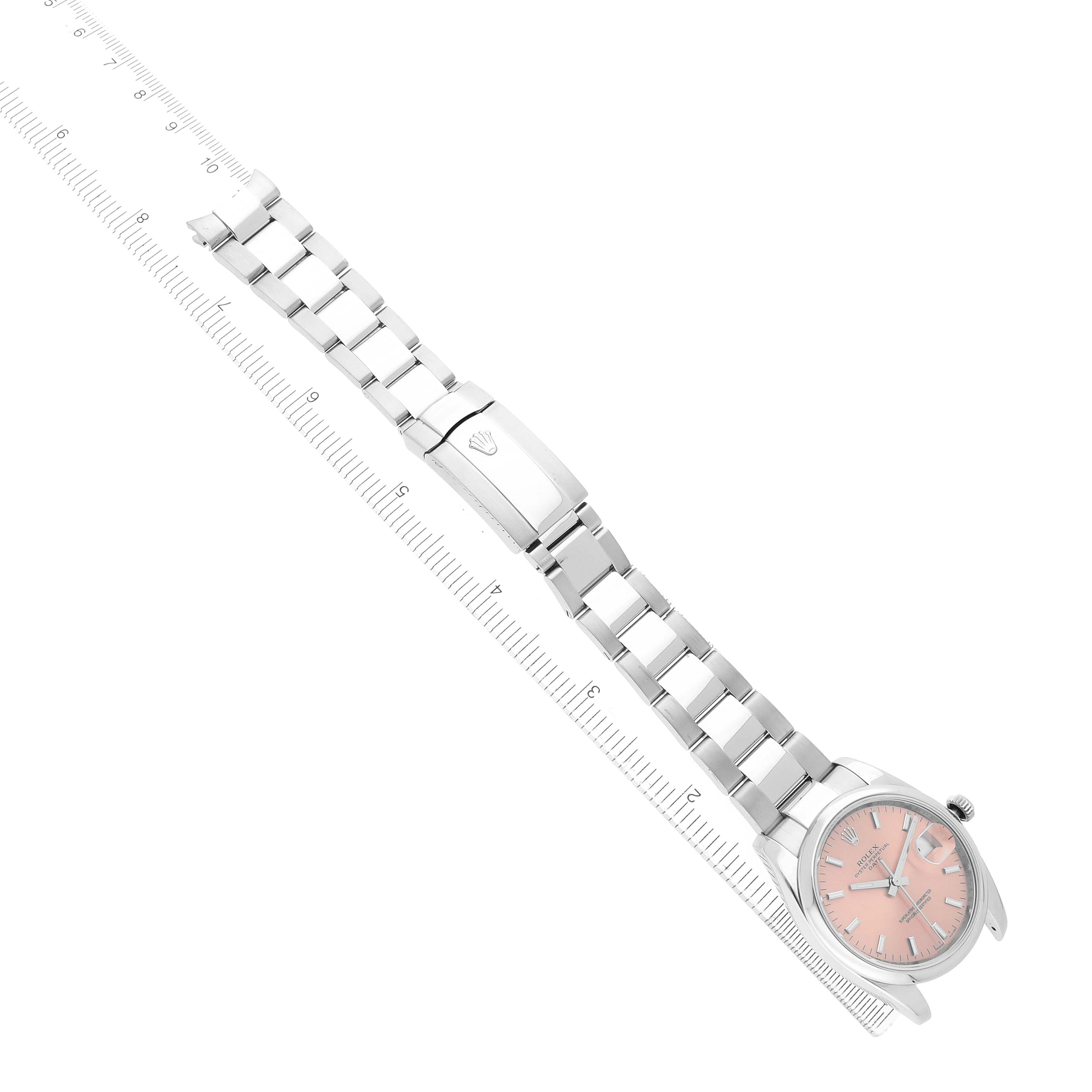 The image shows a Rolex Date 115200 Men's Stainless Steel Pink Dial watch at an angle, featuring its full metal bracelet and pink dial, with a clasp engraved with the logo.