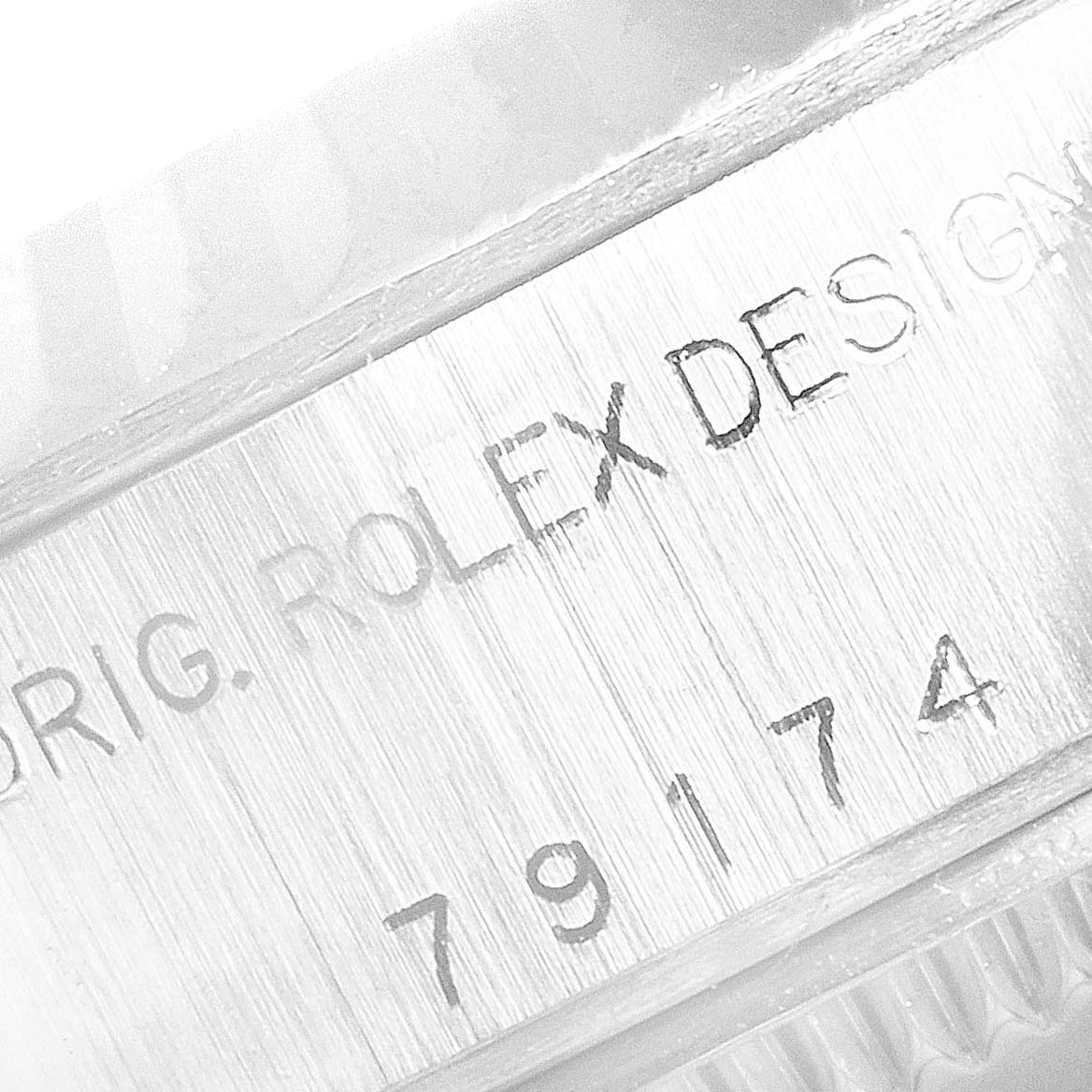 The image shows an engraved serial number and "ORIG. ROLEX DESIGN" on the side of a Rolex Datejust 79174 Women's Stainless Steel White Dial 79174 Women's Stainless Steel White Dial watch case.