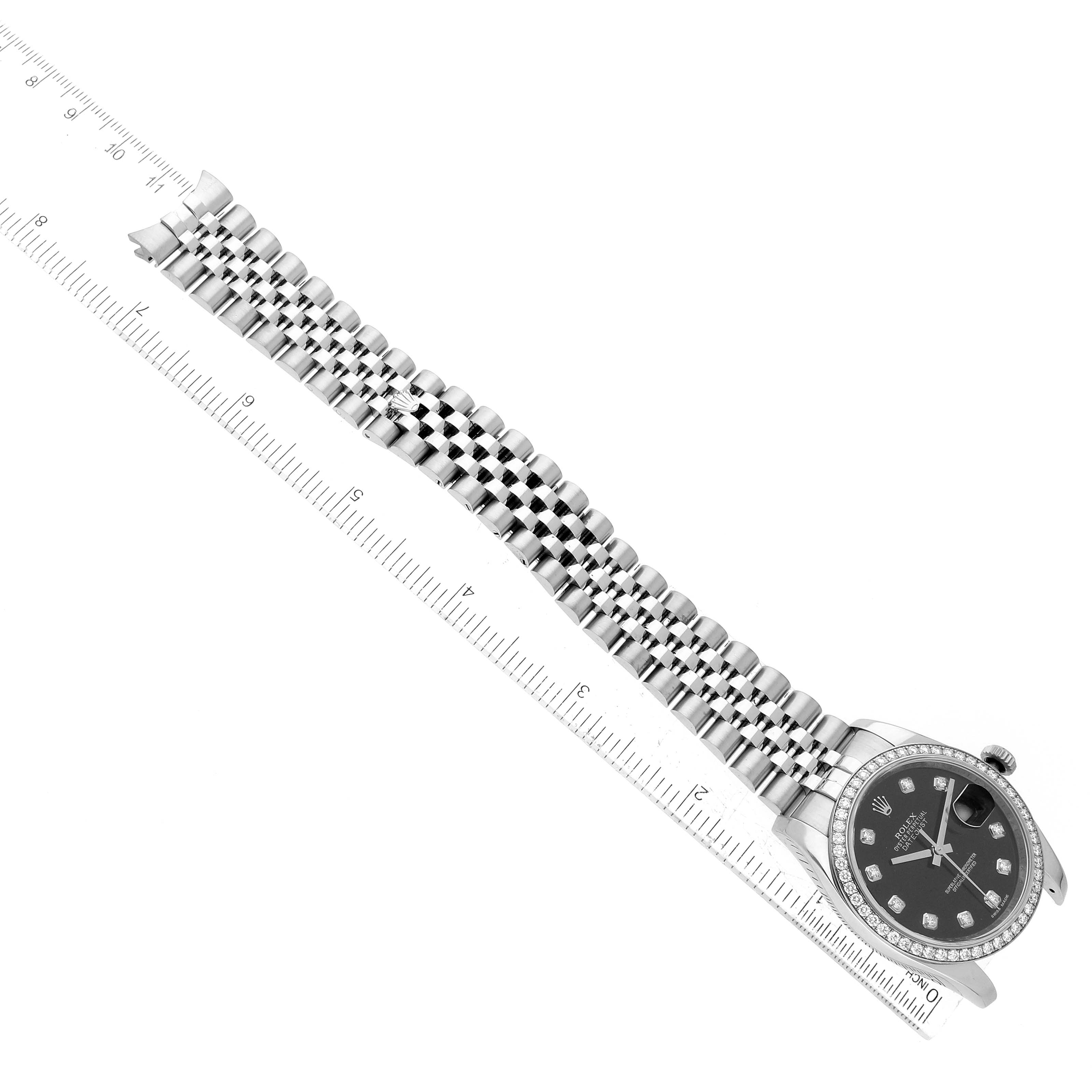 The Rolex Datejust 116244 Men
s Stainless Steel Black Dial 116244 Men
s Stainless Steel Black Dial watch is shown from a top-down angle, highlighting the dial, bezel, and bracelet against a ruler for scale.