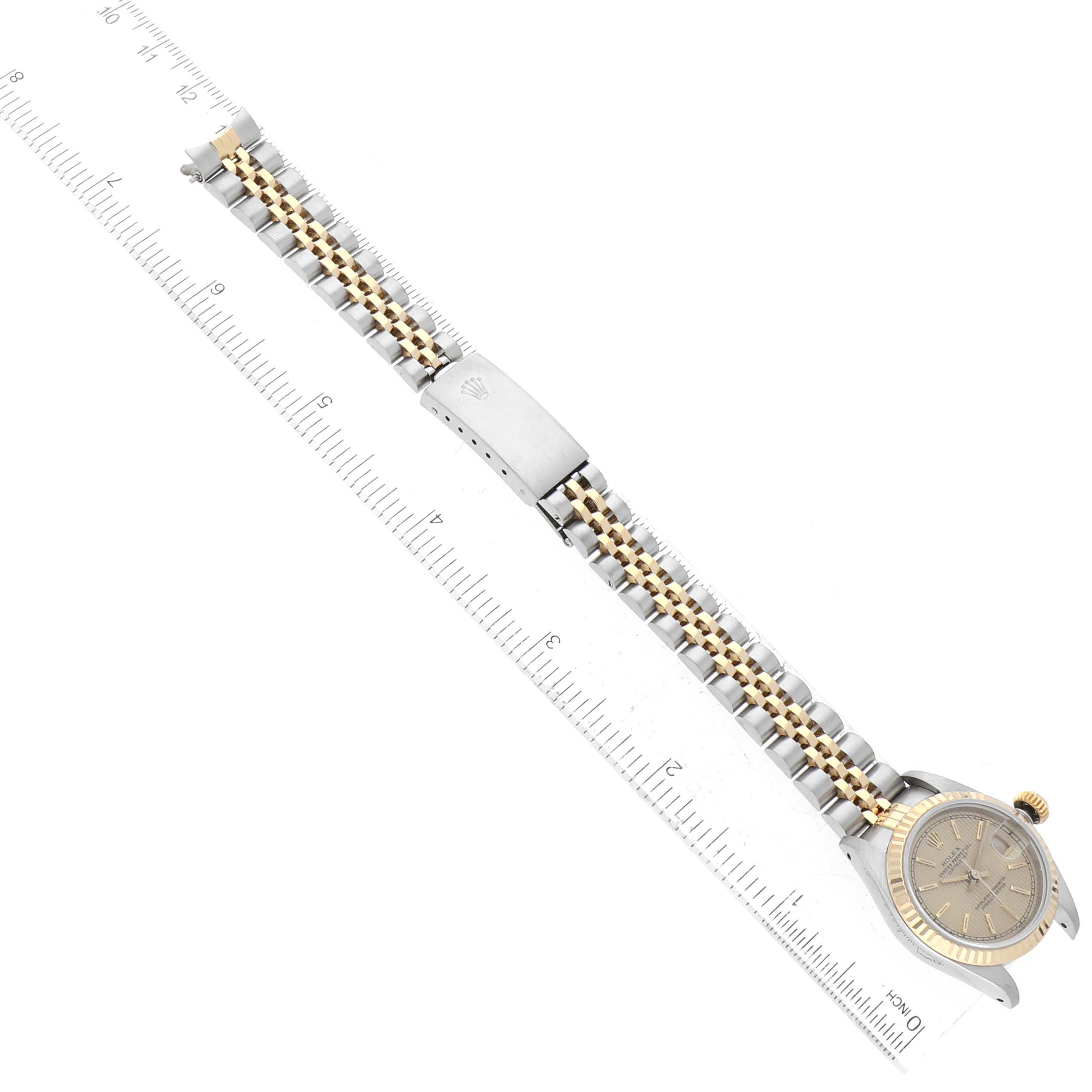 The image shows a top-down view of a Rolex Datejust 69173 Women's Steel and Gold (two tone) Champagne Dial 69173 Women's Steel and Gold (two tone) Champagne Dial watch, displaying its face, bezel, crown, and bracelet lying along a ruler.
