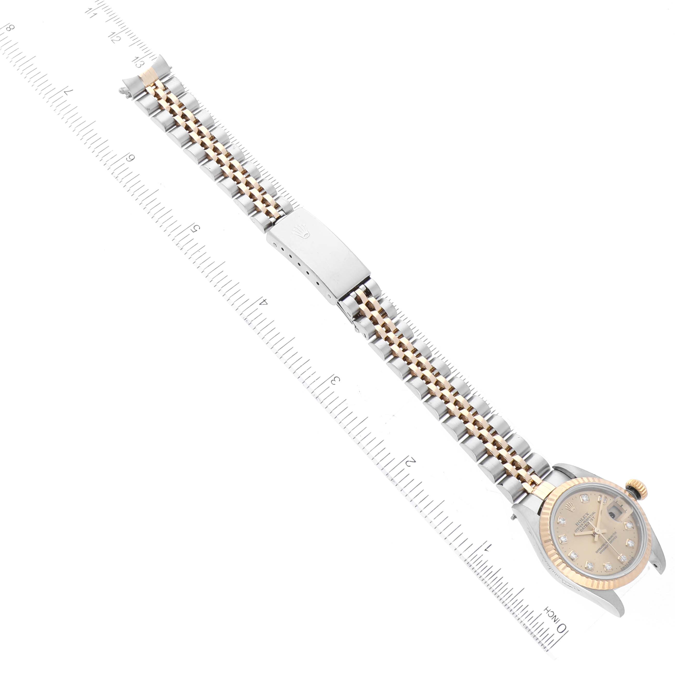 The image shows a Rolex Datejust 79173 Women's Steel and Gold (two tone) Champagne Dial 79173 Women's Steel and Gold (two tone) Champagne Dial watch placed next to a ruler, displaying its face, bracelet, and clasp from a top-down angle.