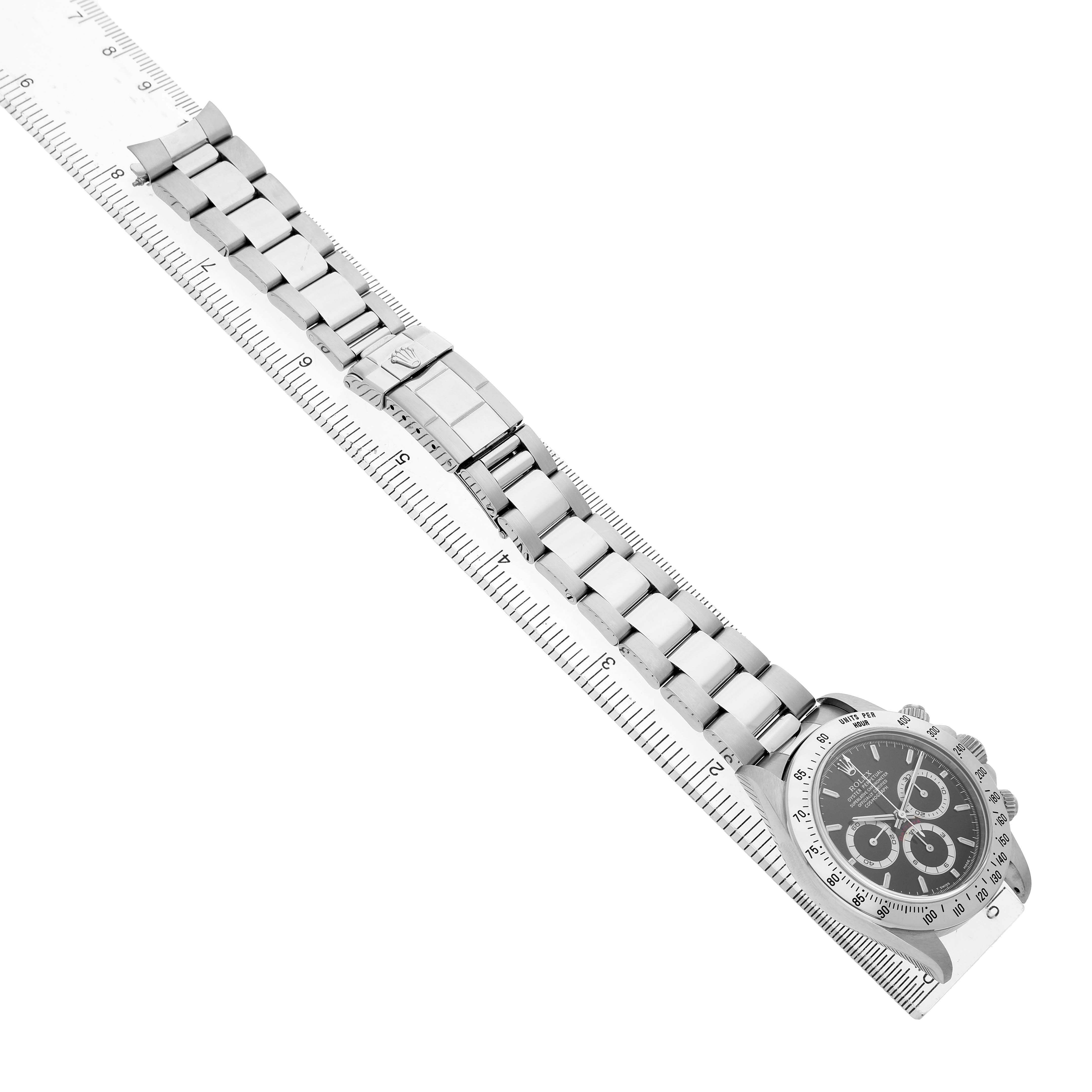 The Rolex Daytona 16520 Men's Stainless Steel Black Dial watch is shown from an angled top view, featuring the full bracelet and clasp alongside a ruler.