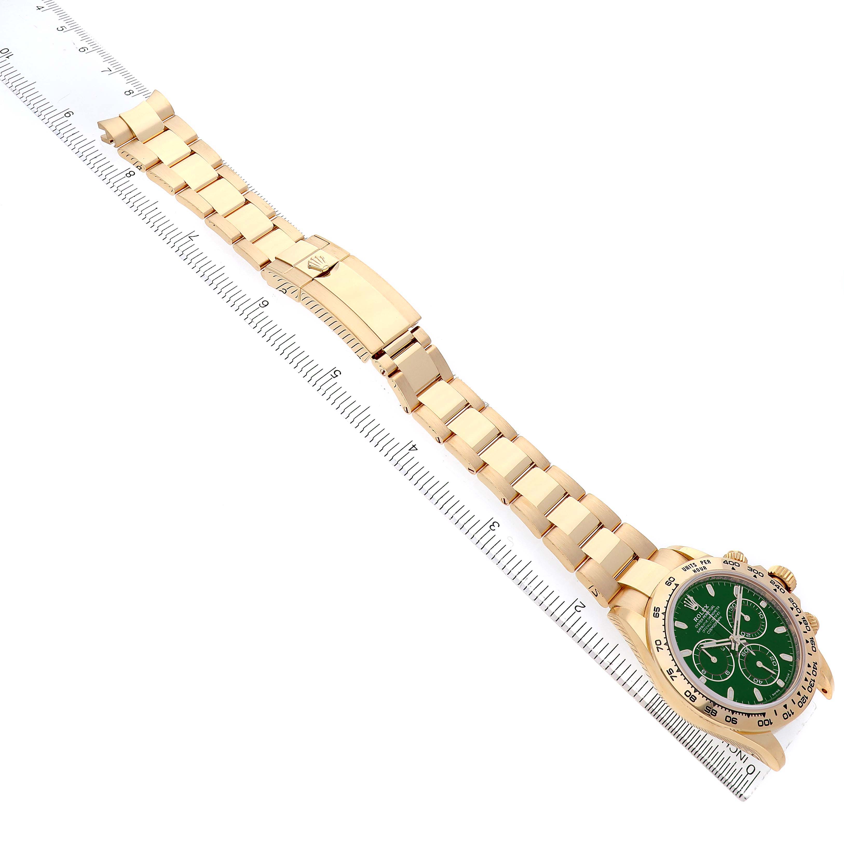 The Rolex Daytona 116508 Men's Yellow Gold Green Dial watch is shown from a top-down angle, displaying the full bracelet and face, resting on a ruler.