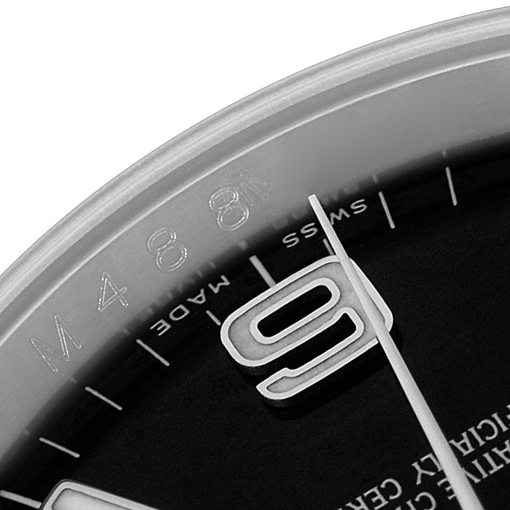 The image shows a close-up of the dial edge and numeral part of a Rolex Oyster Perpetual 116000 Men's Stainless Steel Black Dial watch at an angled view.