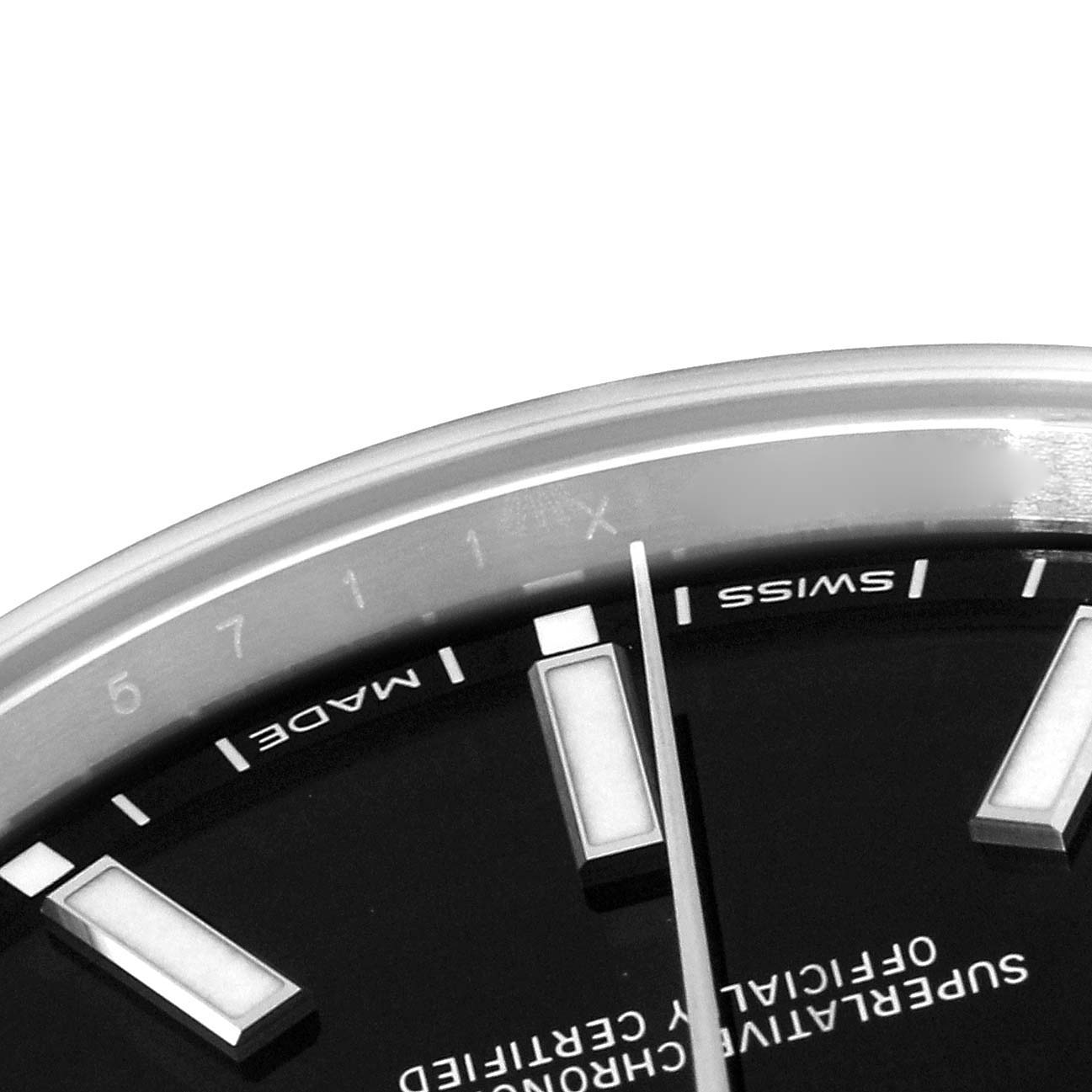The image shows a close-up of the dial and a portion of the bezel of a Rolex Oyster Perpetual 114300 Men's Stainless Steel Black Dial 114300 Men's Stainless Steel Black Dial watch, highlighting the markers and text.