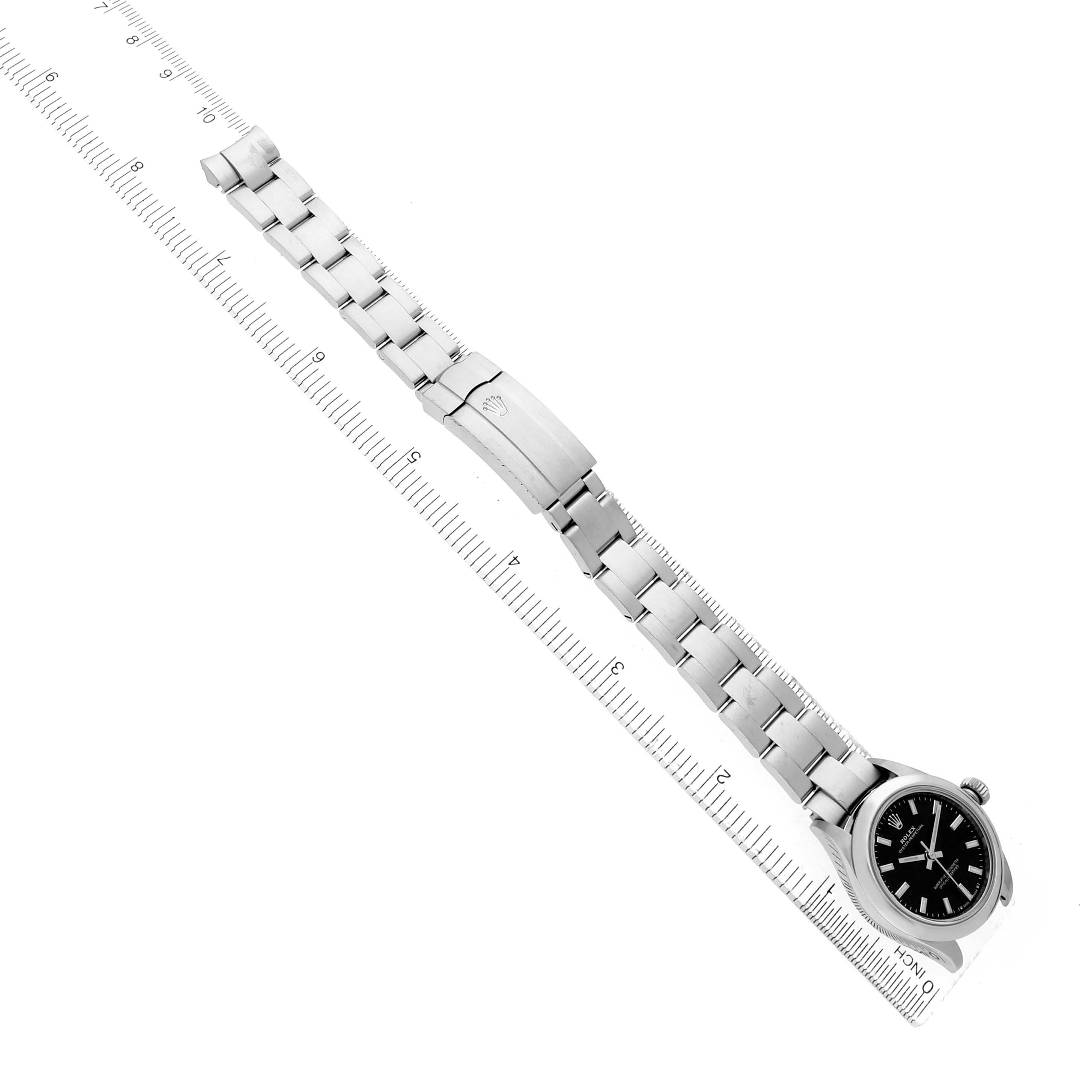 The Rolex Oyster Perpetual 276200 Women's Stainless Steel Black Dial watch is shown from a top-down angle, revealing its black dial, silver bracelet, and clasp.