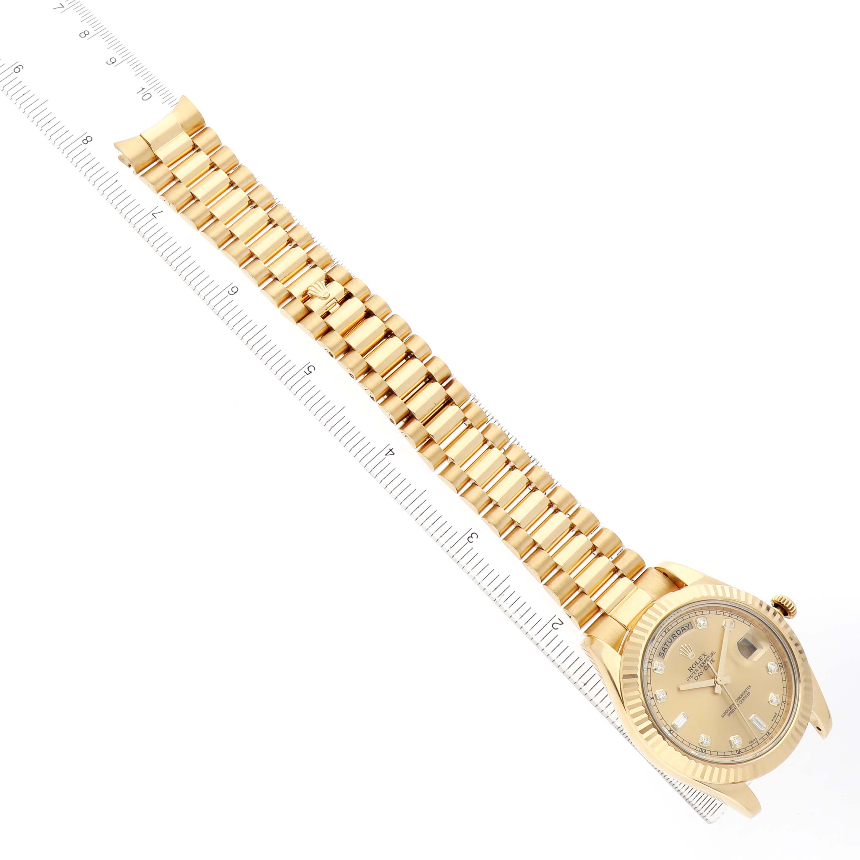 The Rolex President 218238 Men's Yellow Gold Champagne Dial watch is shown at an angled view, featuring its gold strap and face alongside a ruler for scale.