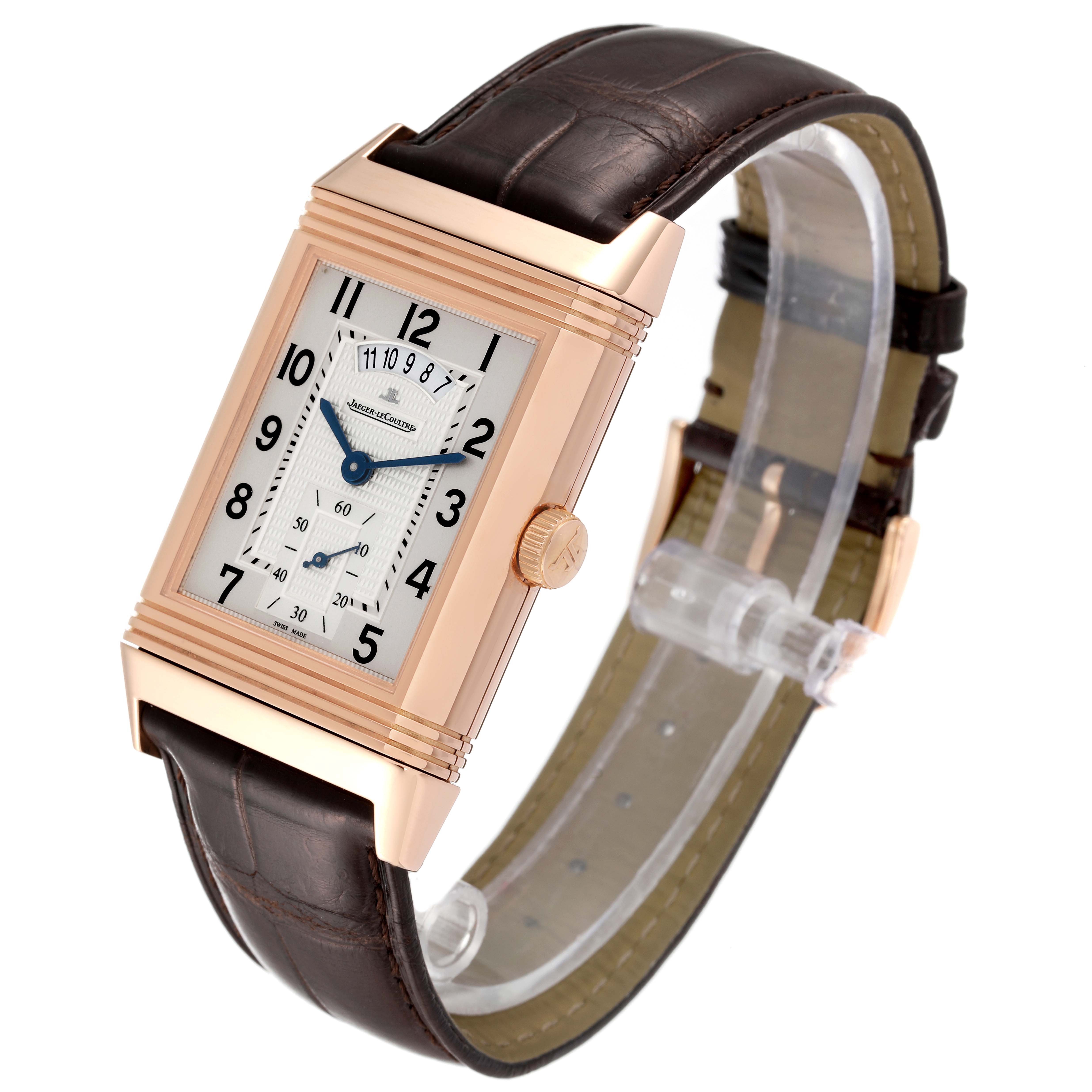 The Jaeger-LeCoultre Reverso watch is shown from an oblique angle, displaying its face, crown, and brown leather strap.