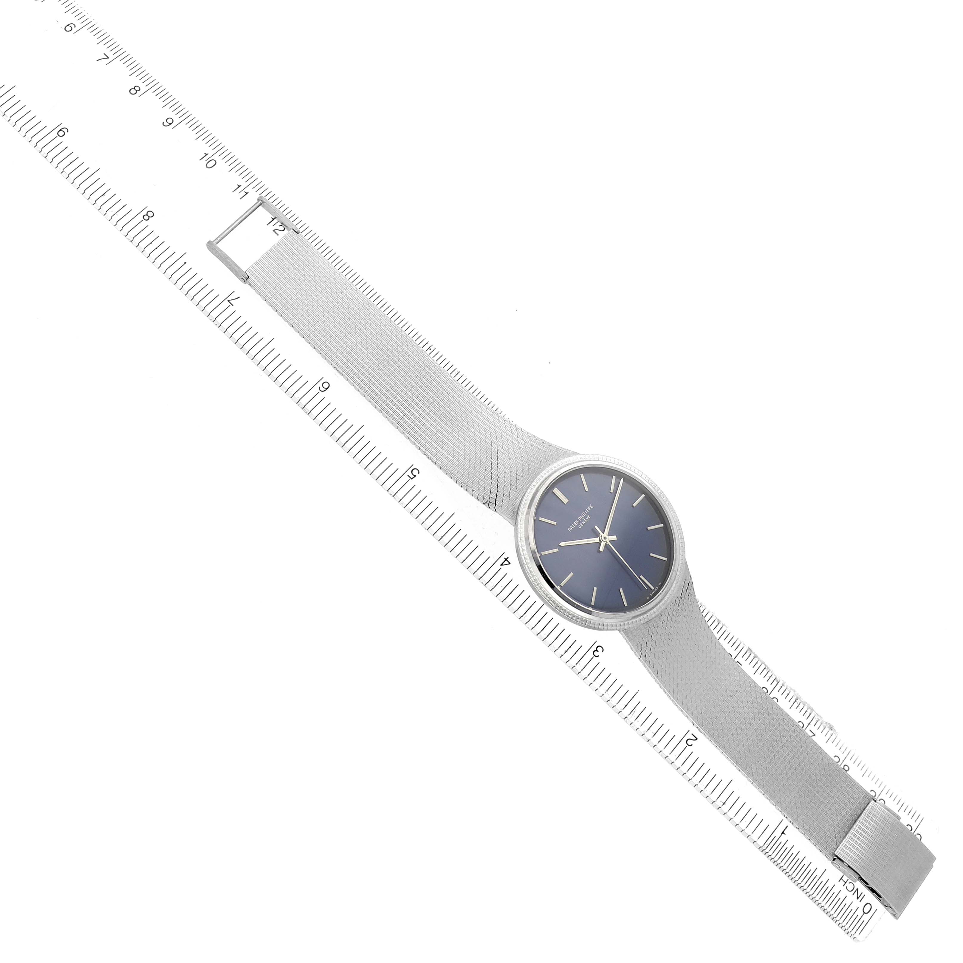 The image shows a Patek Philippe Vintage 3569 Men
s White Gold Blue Dial watch laid diagonally on a ruler, displaying its full face and mesh strap.