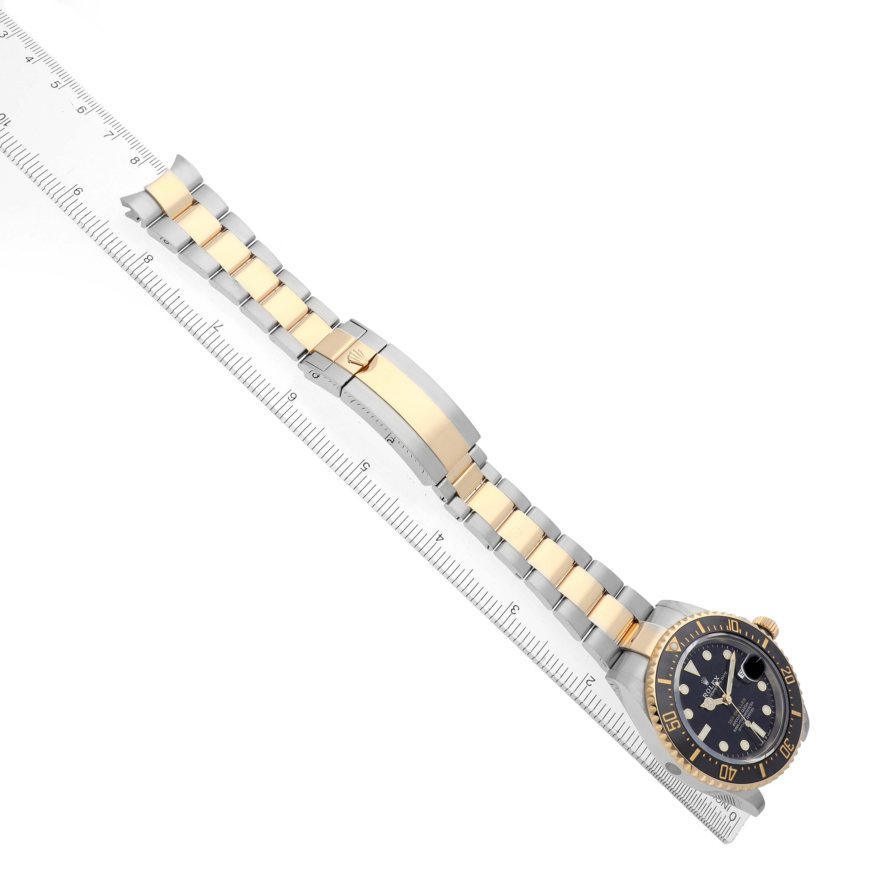 The image shows a Rolex Sea-Dweller 126603 Men
s Steel and Gold (two tone) Black Dial watch and its bracelet laid diagonally with a ruler beneath.