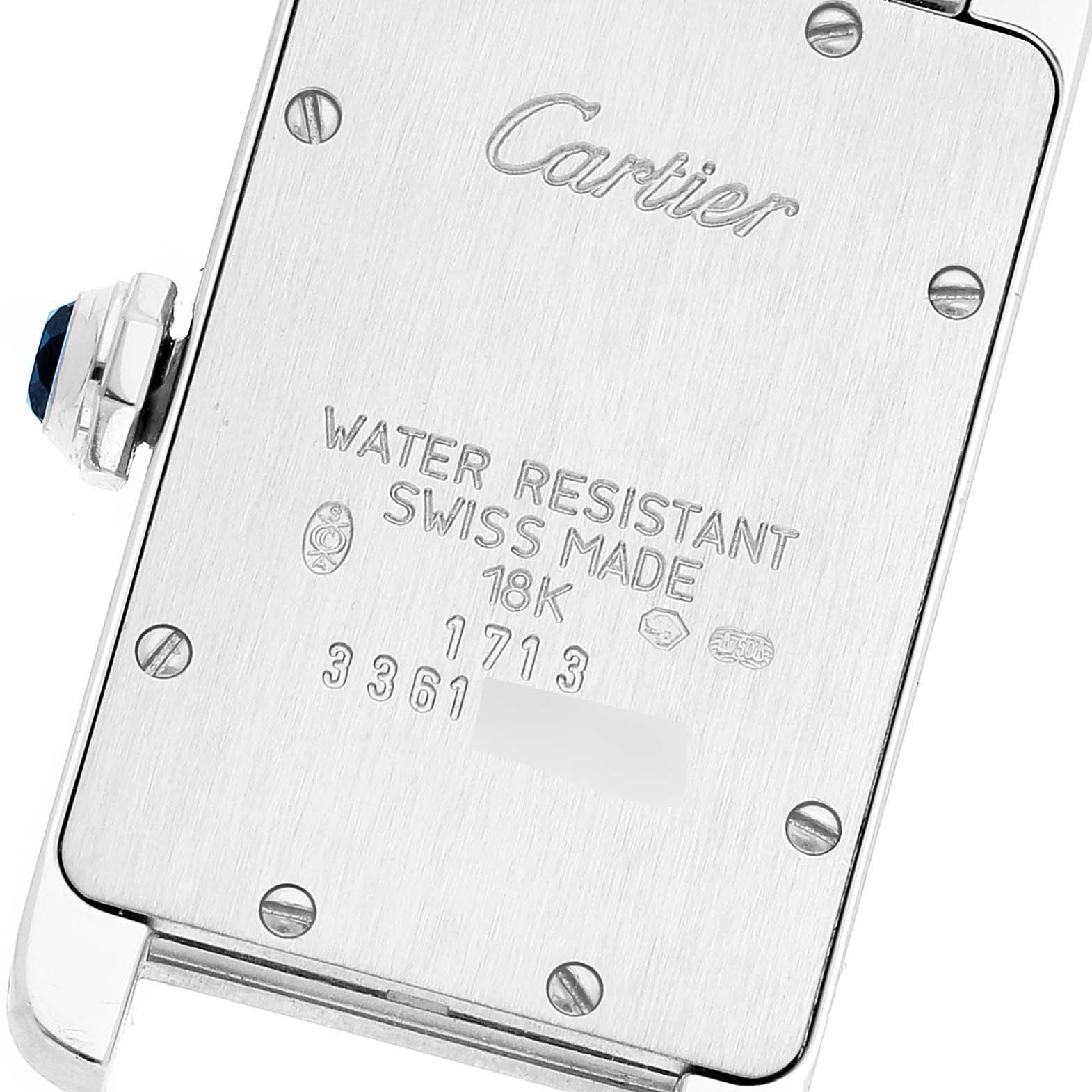 The image shows the back case of a Cartier Tank Americaine W008067 Women's White Gold Silver Dial W008067 Women's White Gold Silver Dial watch, featuring inscriptions and a visible crown with a blue jewel.