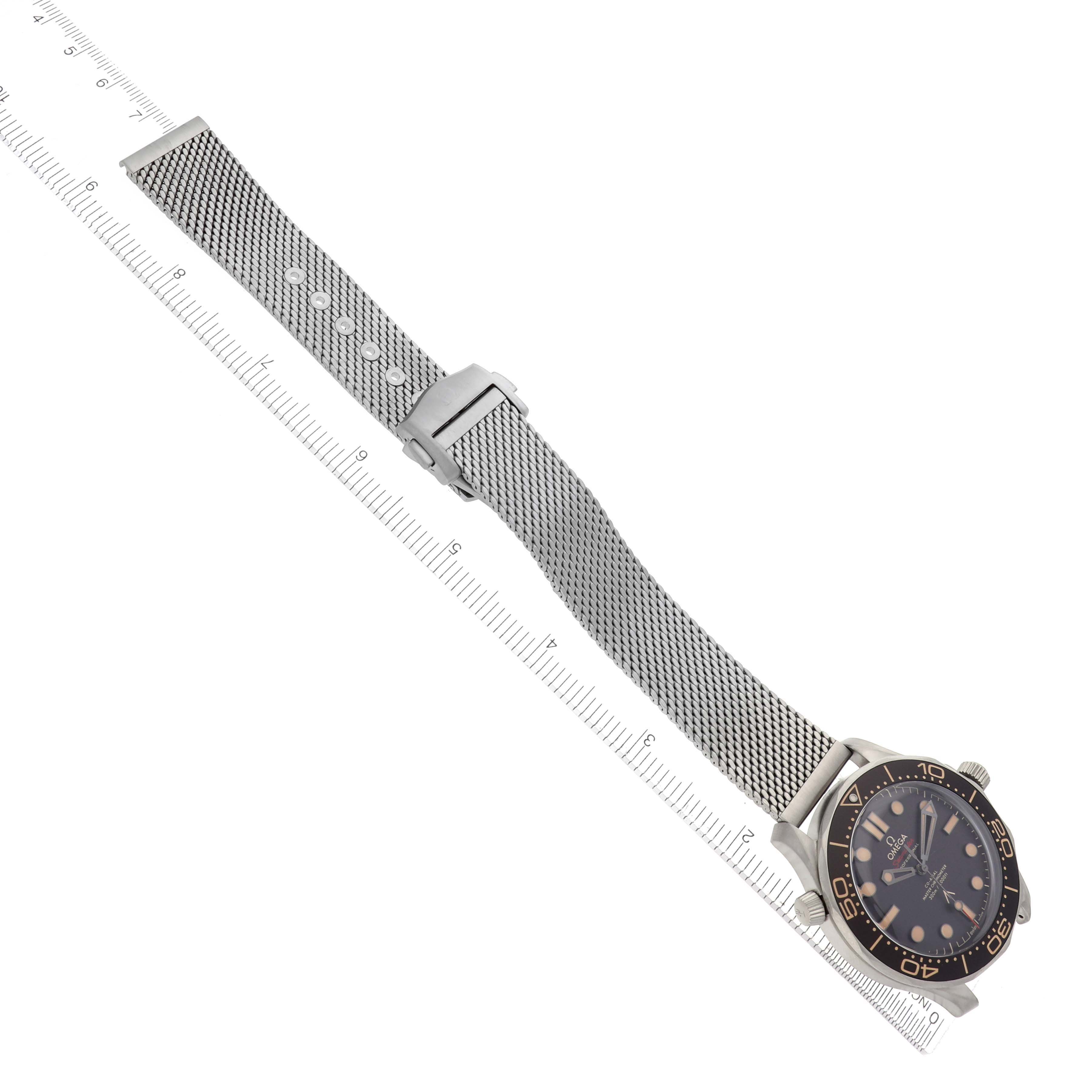The image shows an Omega Seamaster 210.92.42.20.01.001 Men's Titanium Brown Dial watch at a diagonal angle with a mesh strap and clasp, displayed beside a ruler.