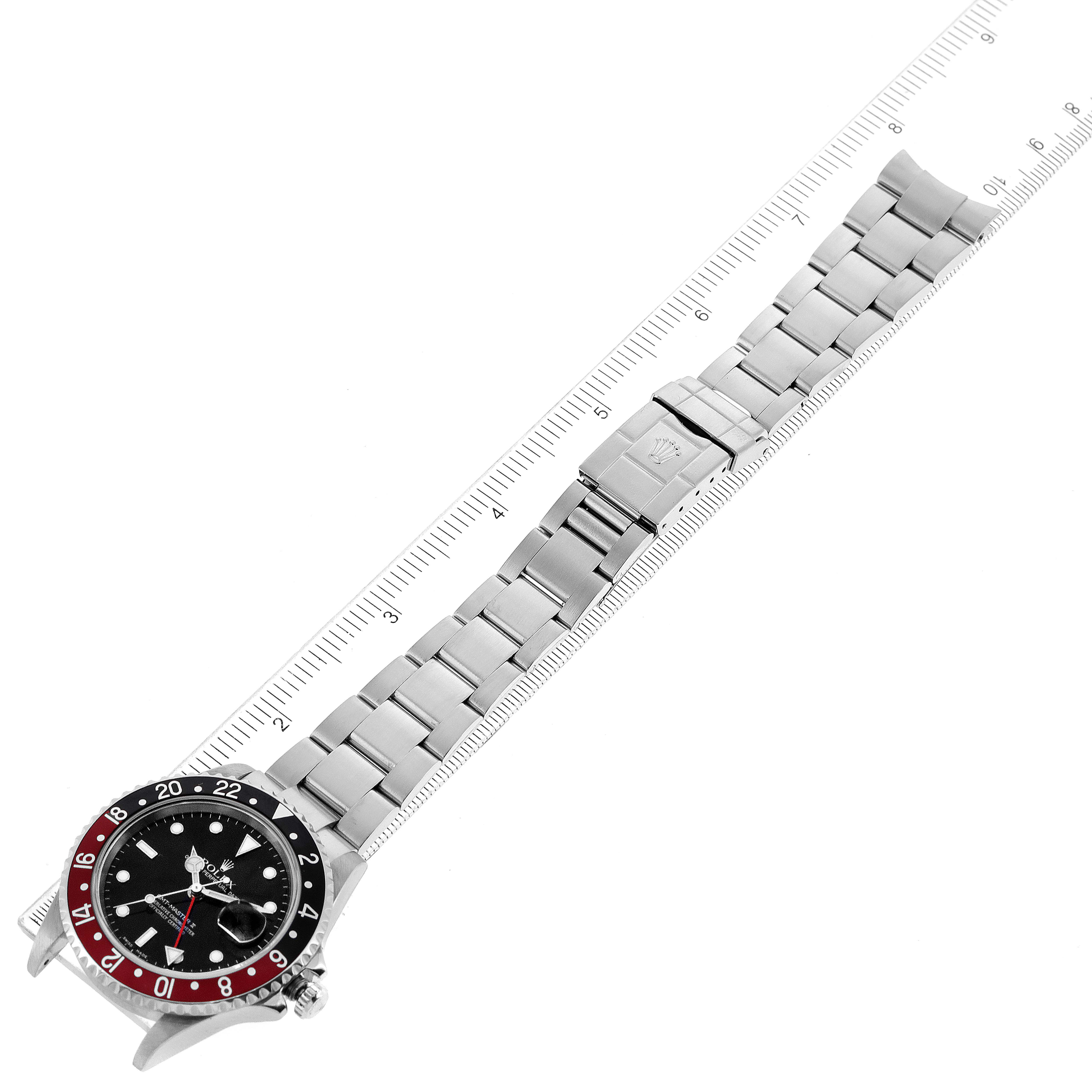 The image shows a top view of the Rolex GMT-Master 16710 Men
s Stainless Steel Black Dial 16710 Men
s Stainless Steel Black Dial watch, displaying the face, bezel, and full metal bracelet next to a ruler.