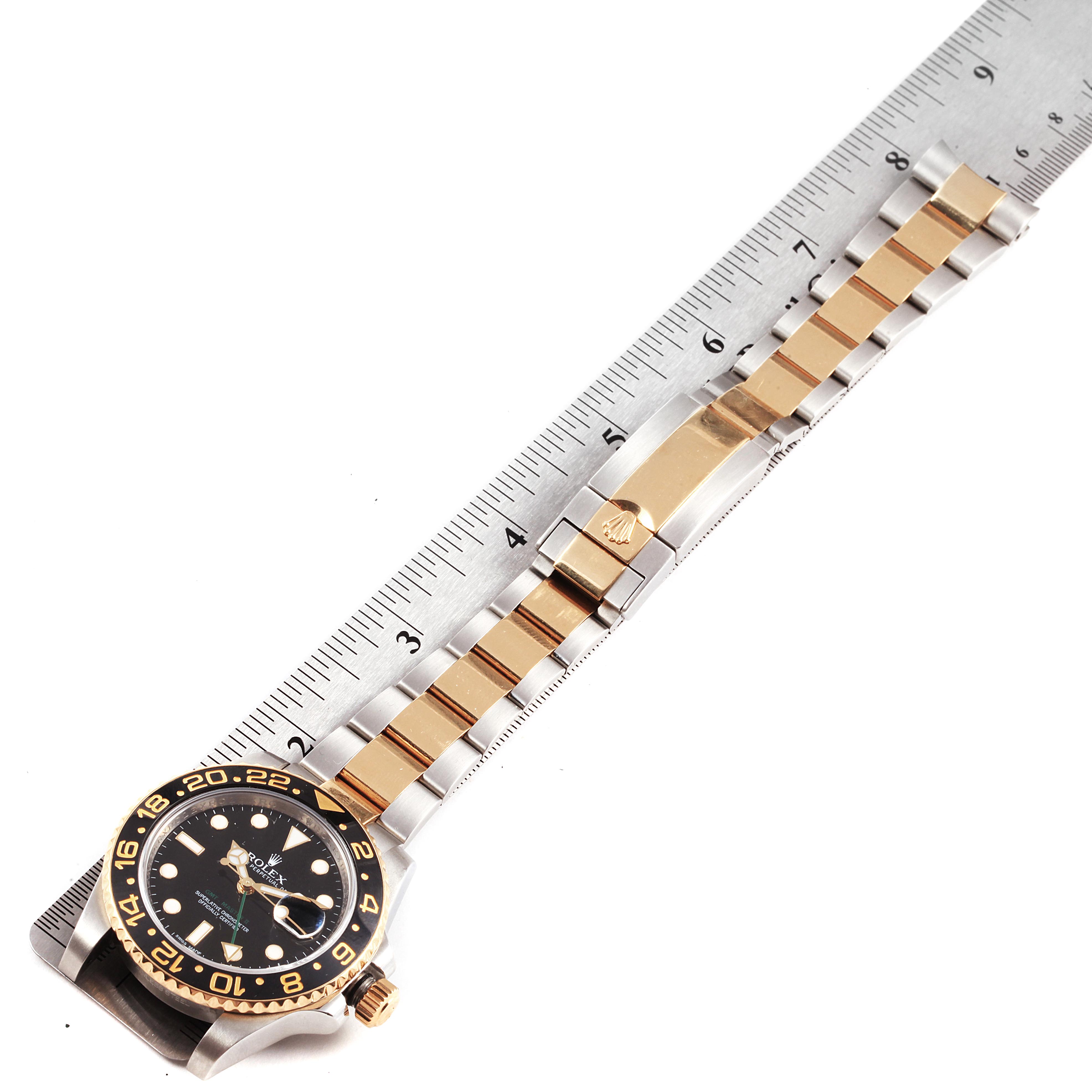 The image shows a top view of a Rolex GMT-Master 116713 Men's Steel and Gold (two tone) Black Dial 116713 Men's Steel and Gold (two tone) Black Dial watch lying on a ruler, displaying the face, bezel, and metal bracelet.