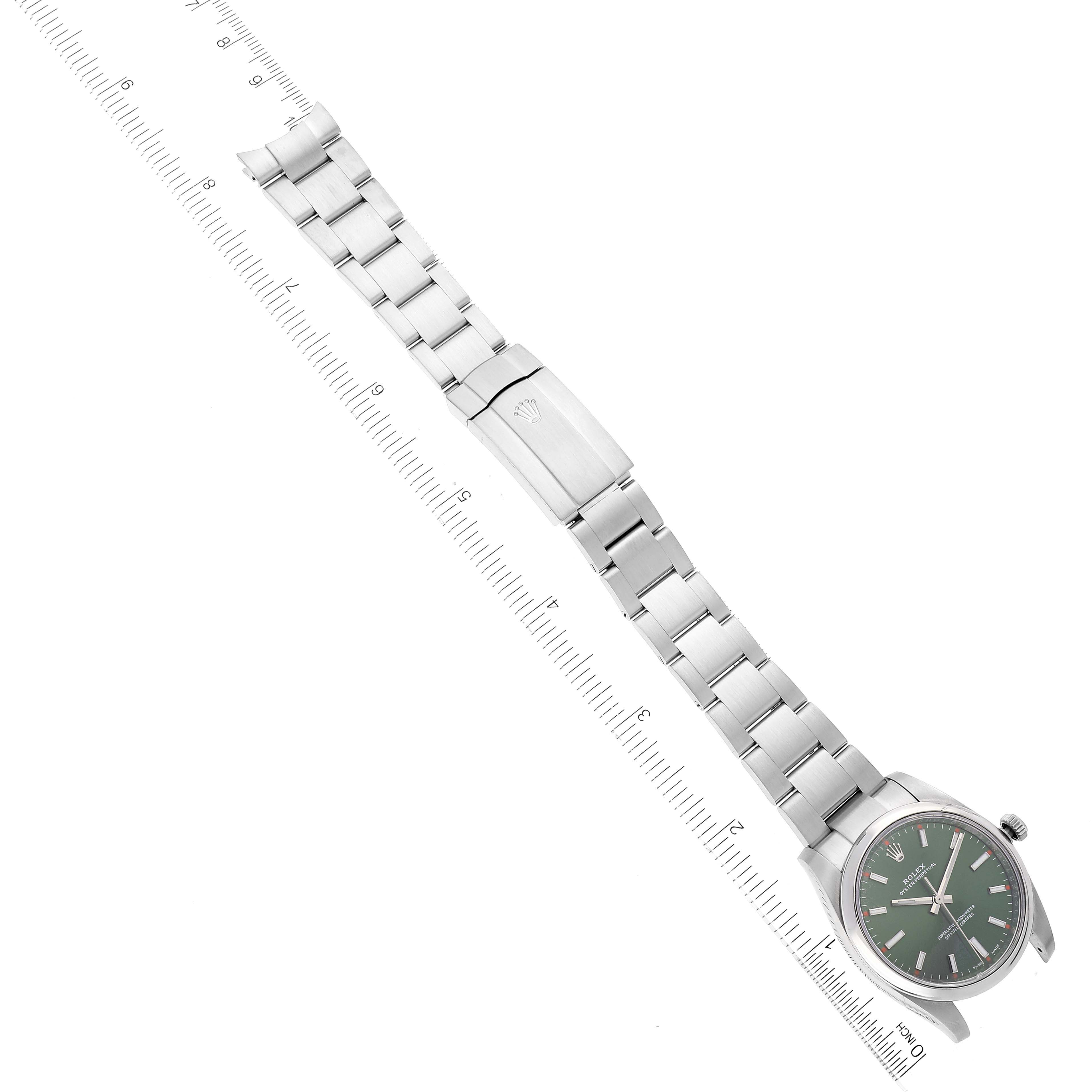 The image shows a Rolex Oyster Perpetual 114200 Men's Stainless Steel Green Dial 114200 Men's Stainless Steel Green Dial watch laid out flat, highlighting the strap, clasp, and watch face, with a ruler alongside it.