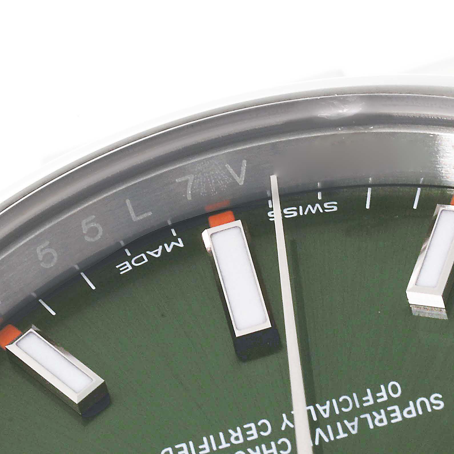 This image shows the upper part of the dial and partial bezel of the Rolex Oyster Perpetual 114200 Men's Stainless Steel Green Dial 114200 Men's Stainless Steel Green Dial watch, revealing index markers and text.