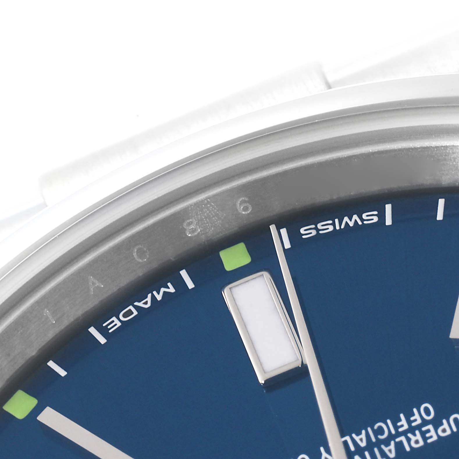 The image shows a close-up of the dial and edge of the bezel of a Rolex Oyster Perpetual 114300 Men's Stainless Steel Blue Dial 114300 Men's Stainless Steel Blue Dial watch.