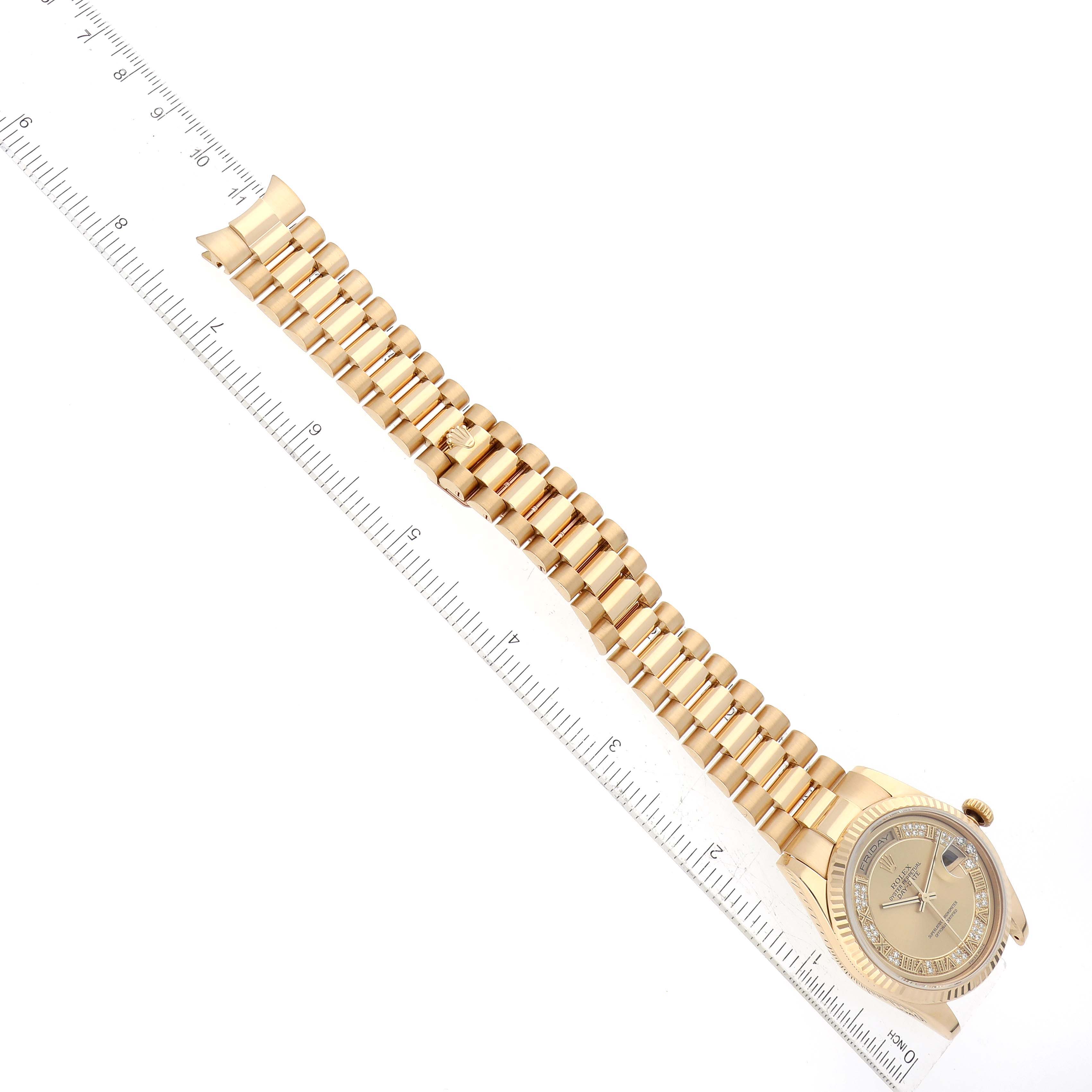 The image shows a Rolex President 118238 Men
s Yellow Gold Champagne Dial 118238 Men
s Yellow Gold Champagne Dial model watch laid flat with a ruler alongside it, displaying the gold bracelet and partial view of the watch face.
