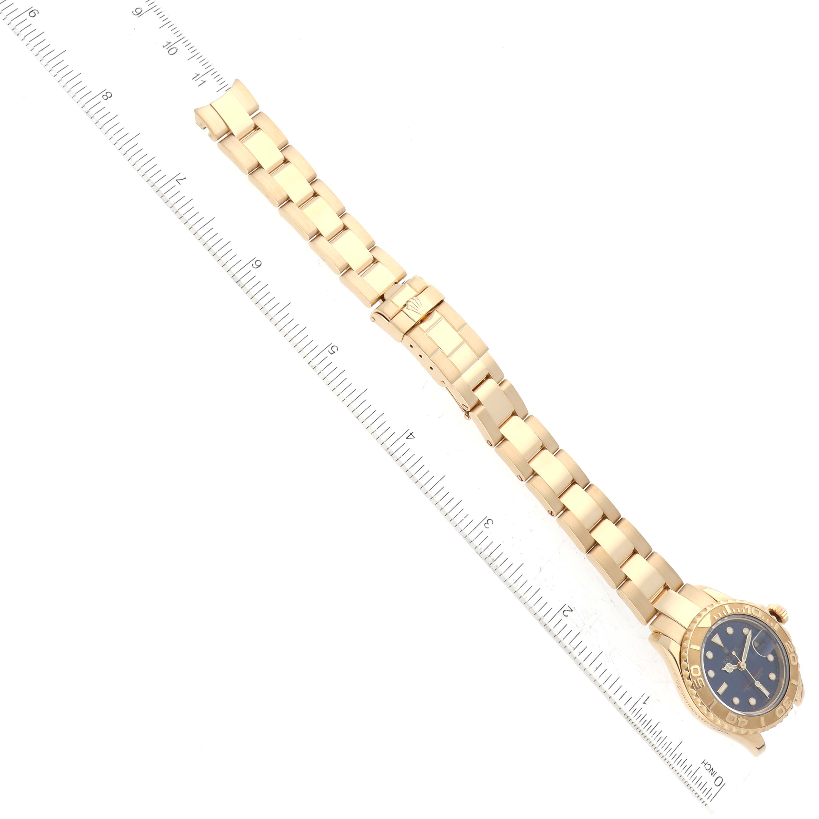 The image shows a Rolex Yacht-Master 69628 Women's Yellow Gold Blue Dial 69628 Women's Yellow Gold Blue Dial watch placed flat with its bracelet extended, positioned next to a ruler for scale.