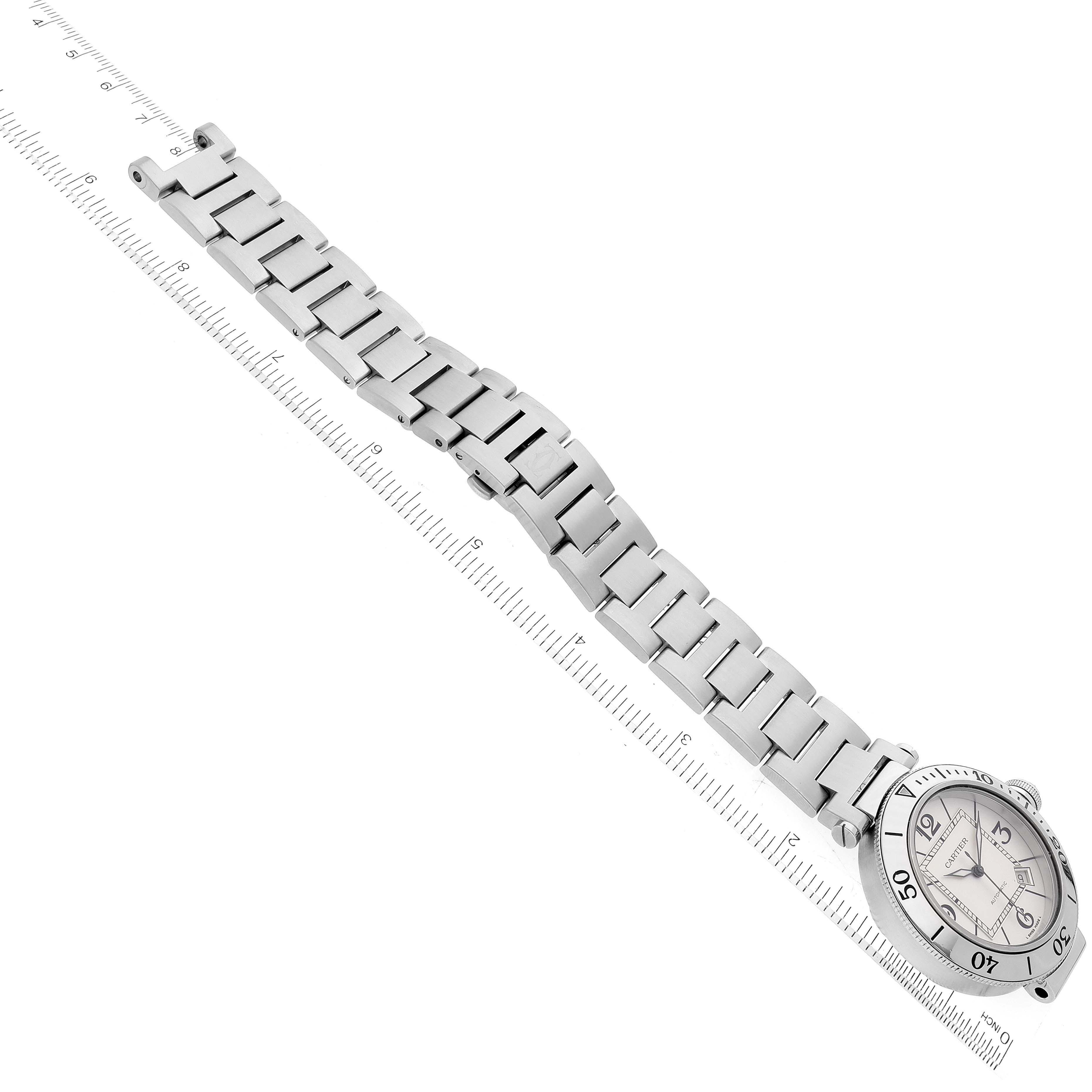 The image shows a Pasha model watch by Cartier laid flat at a slight angle, highlighting its face and metal bracelet with a ruler next to it.