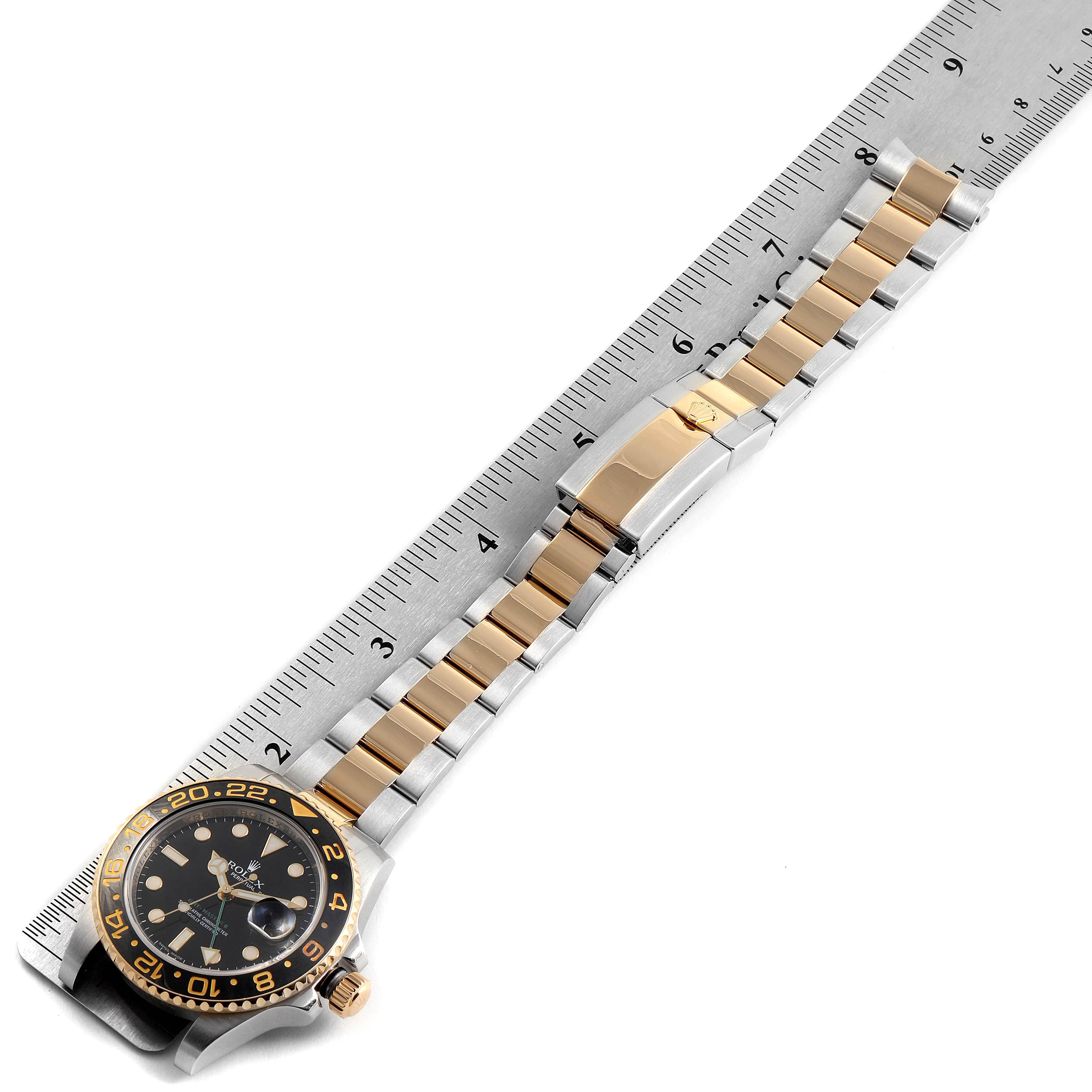 This image shows a Rolex GMT-Master 116713 Men's Steel and Gold (two tone) Black Dial 116713 Men's Steel and Gold (two tone) Black Dial watch laid alongside a ruler, showcasing its bracelet, clasp, and dial.