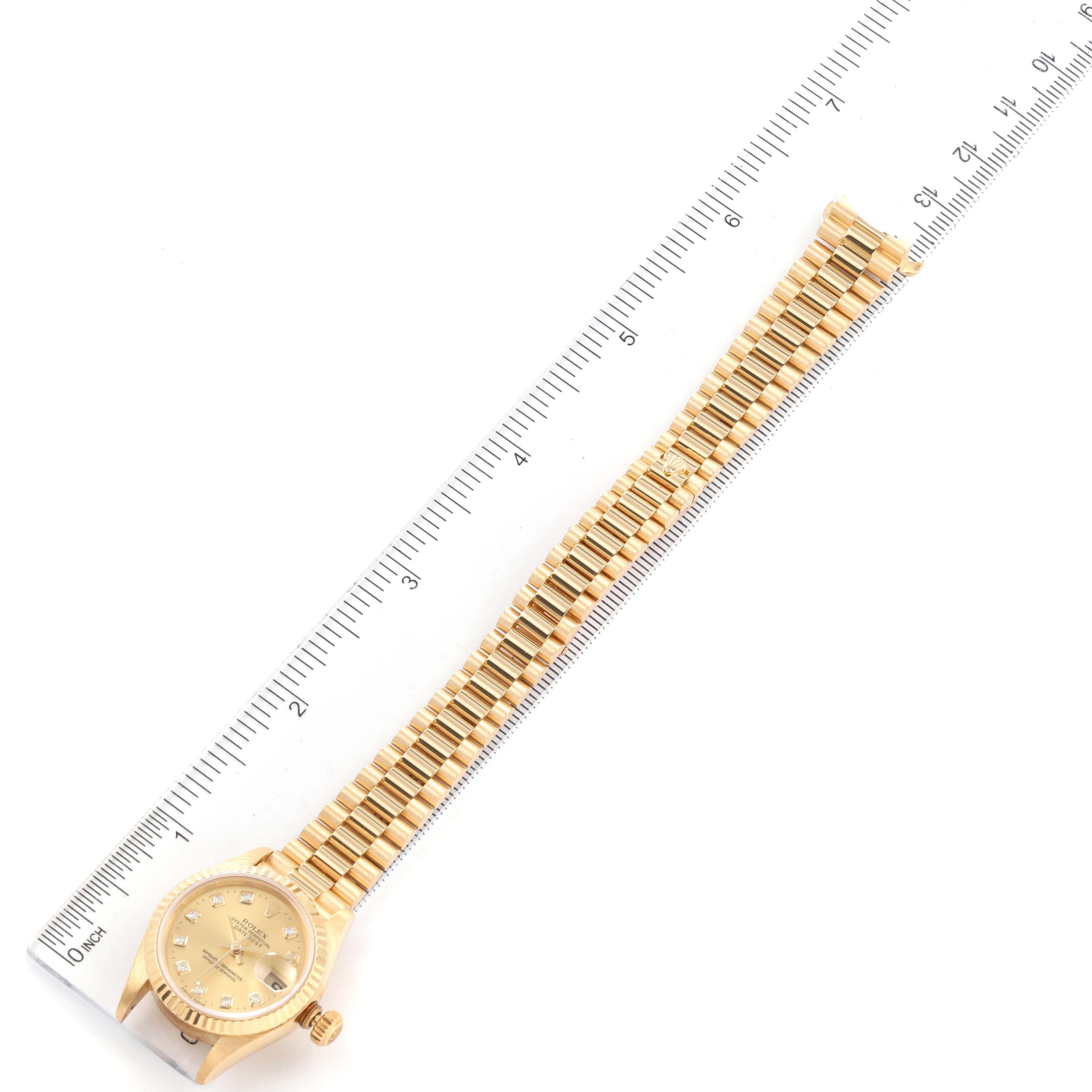 This image shows a Rolex President 79178 Women
s Yellow Gold Champagne Dial 79178 Women
s Yellow Gold Champagne Dial model watch, positioned diagonally with its face and entire gold bracelet visible alongside a ruler.