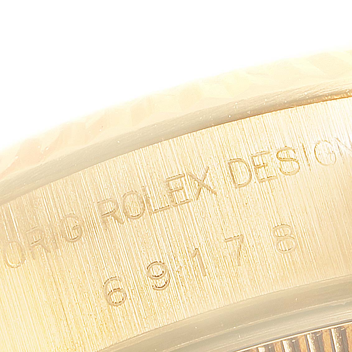 This close-up image shows the edge of the case of a Rolex President 69178 Women's Yellow Gold Champagne Dial 69178 Women's Yellow Gold Champagne Dial model watch with engraved text.