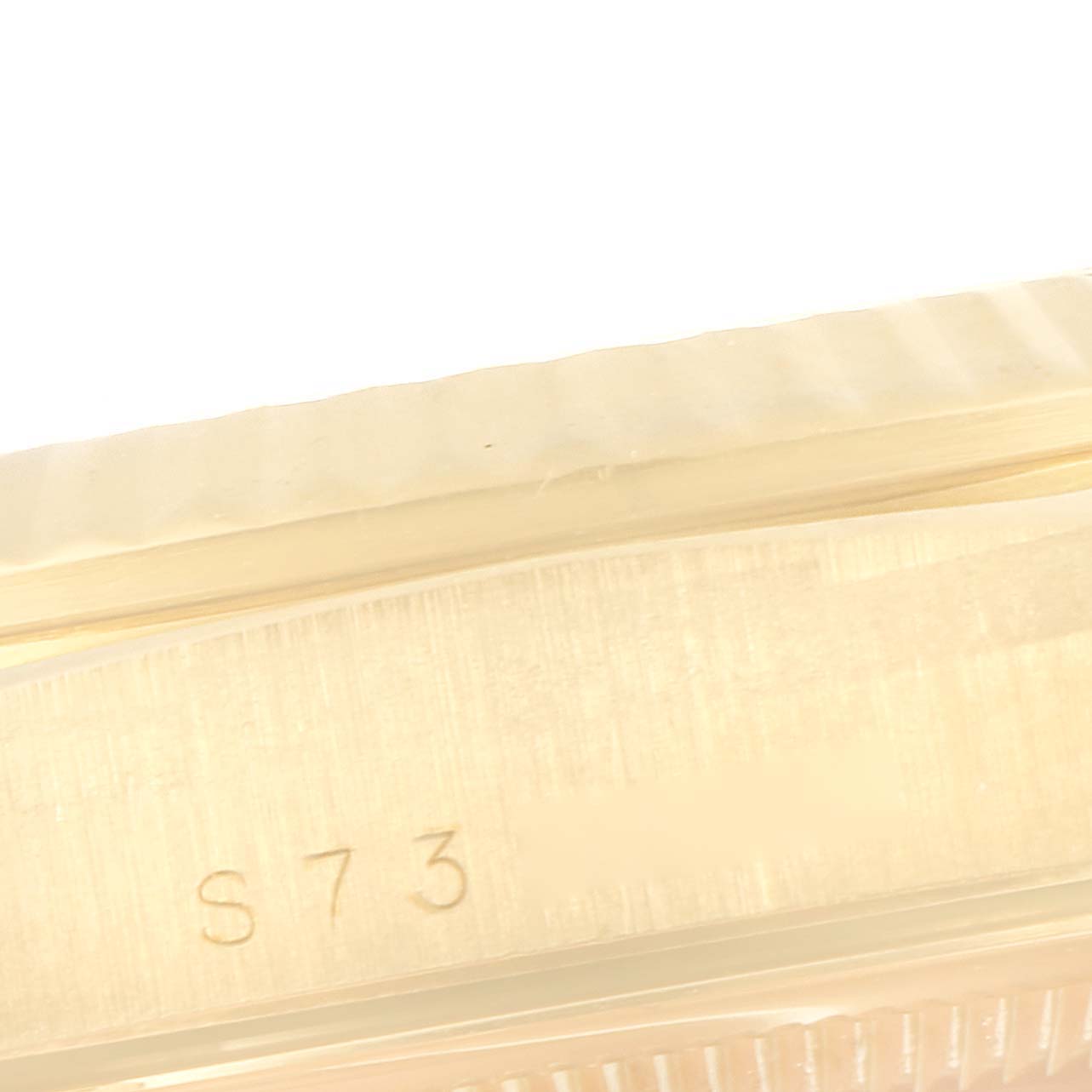 A close-up of the Rolex President 18238 Men
s Yellow Gold Champagne Dial 18238 Men
s Yellow Gold Champagne Dial model watch
s fluted bezel and part of the case with the engraving "S73".