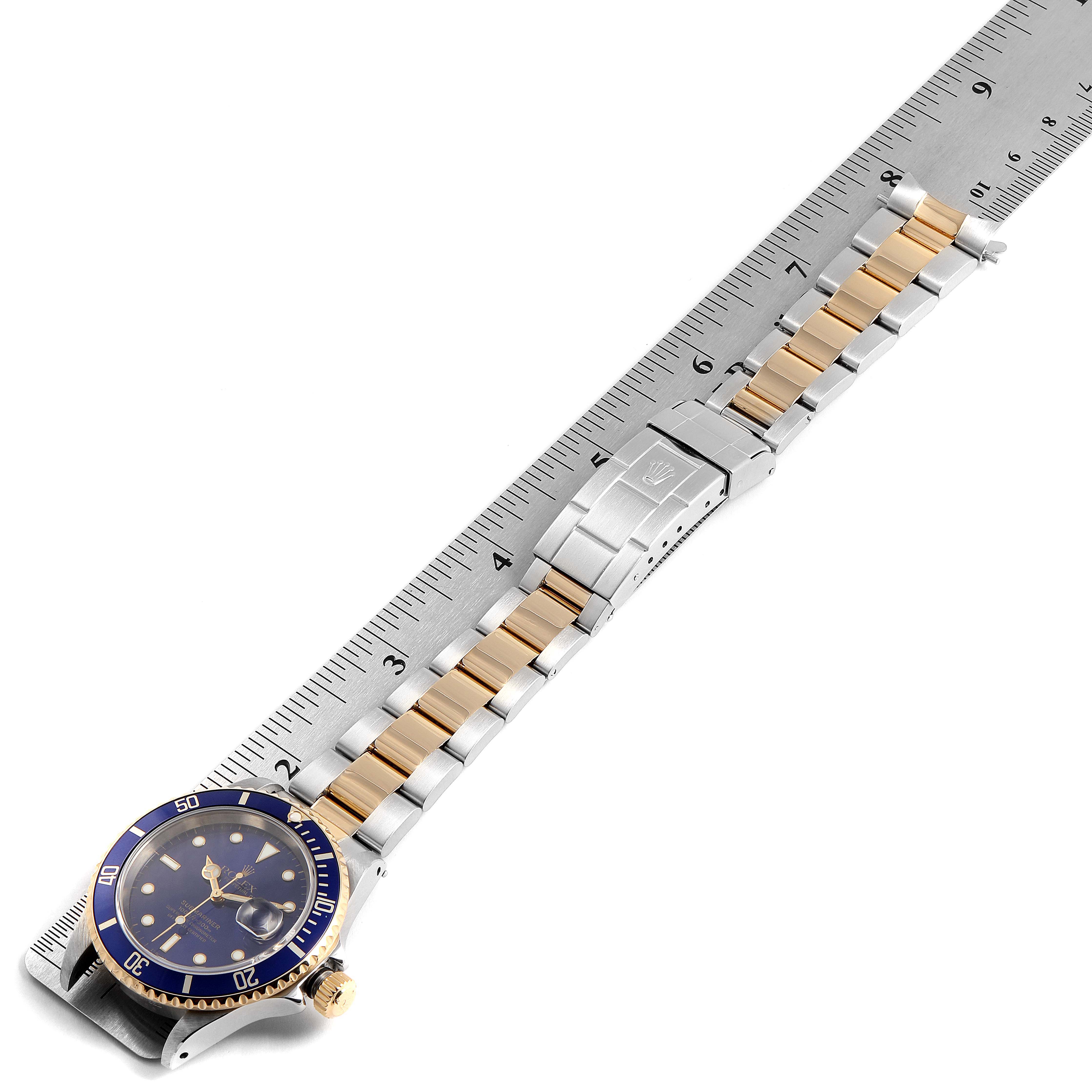 The image shows the Rolex Submariner 16613 Men's Steel and Gold (two tone) Blue Dial 16613 Men's Steel and Gold (two tone) Blue Dial watch laid flat, displaying the face, bezel, bracelet, and clasp, aligned with a ruler.