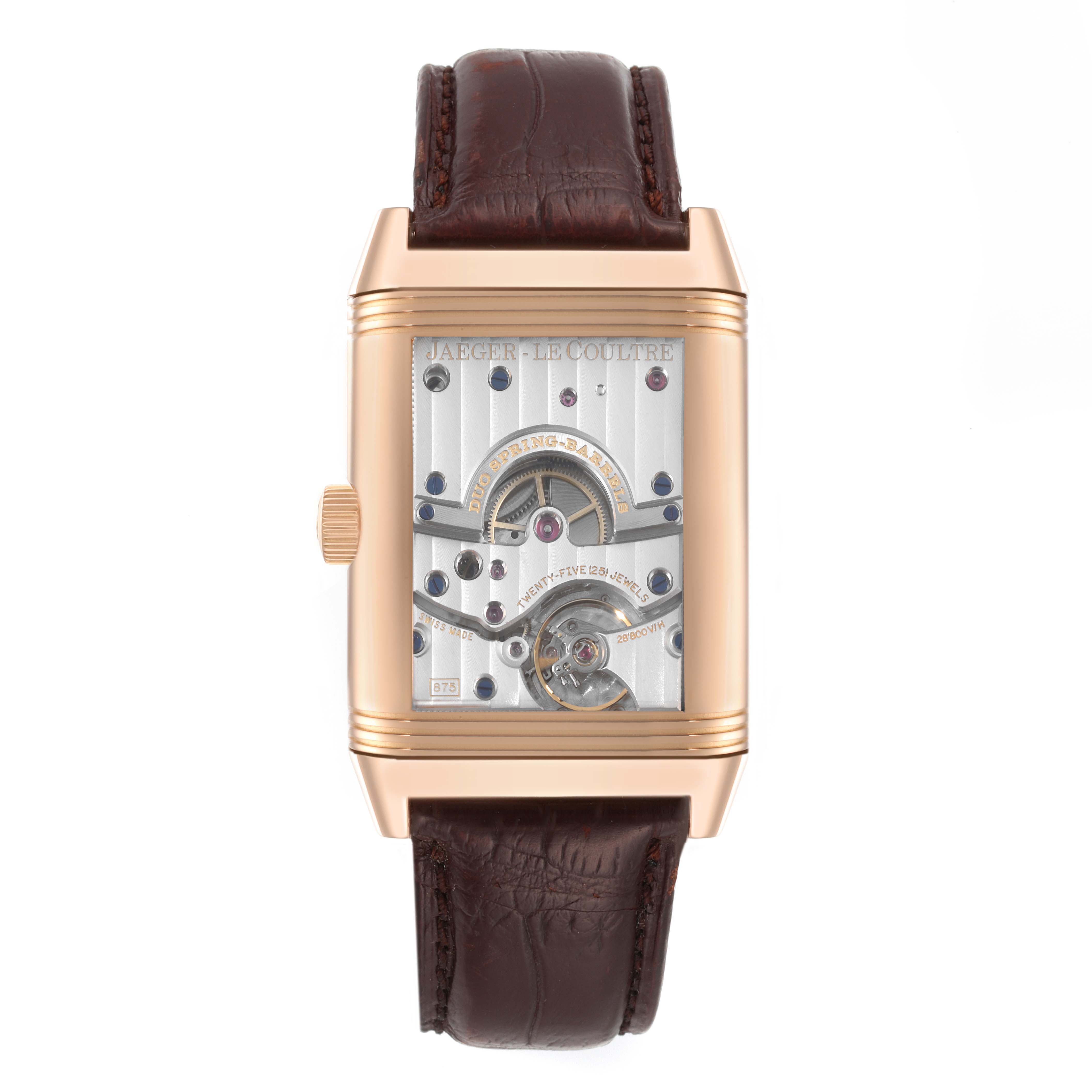 The Jaeger-LeCoultre Reverso watch is shown from the front, highlighting its movement mechanism and brown leather strap.