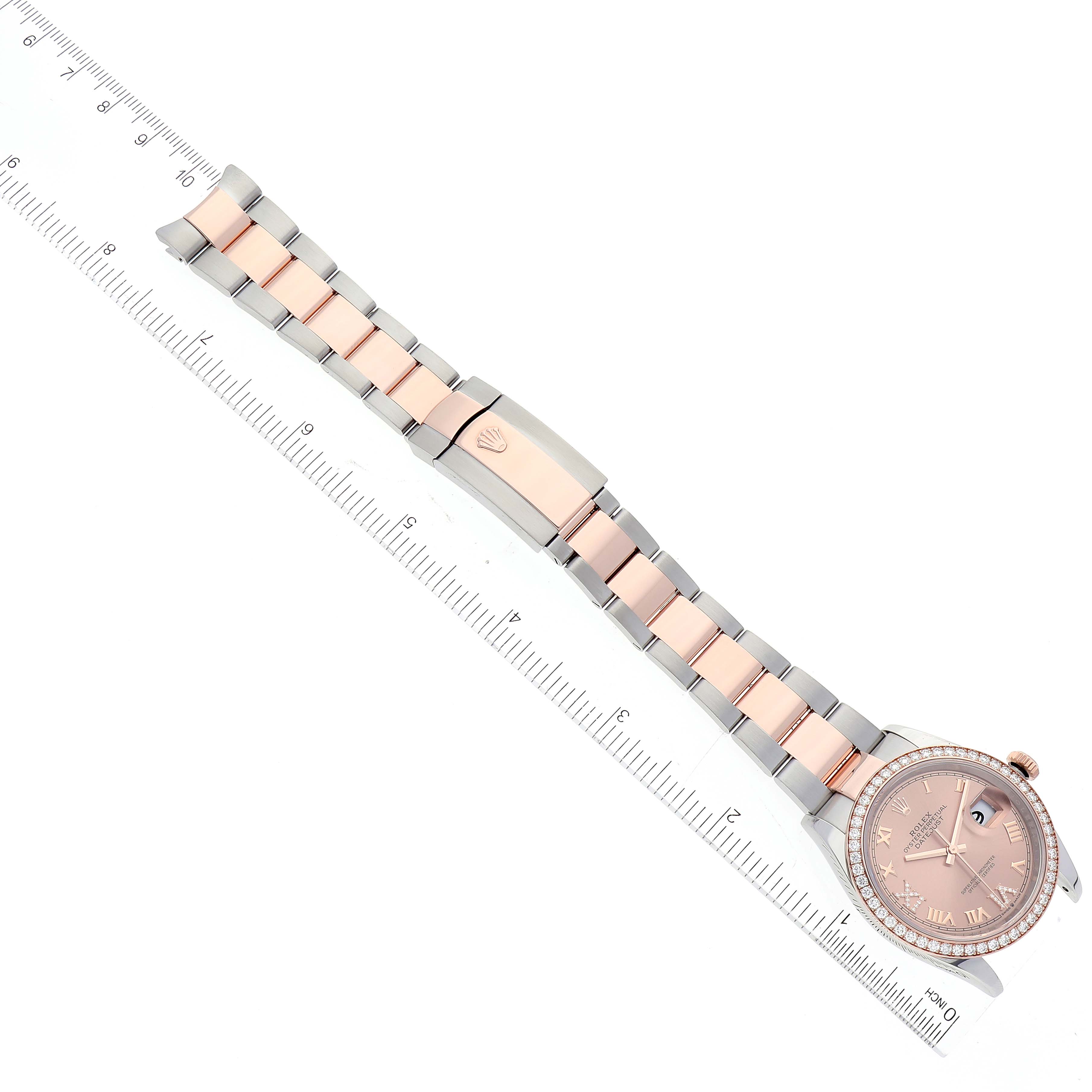 The Rolex Datejust 126281 Men's Steel and Gold (two tone) Pink Dial 126281 Men's Steel and Gold (two tone) Pink Dial watch is shown at a top-down angle, featuring the bezel, dial, bracelet, and clasp alongside a ruler for scale.