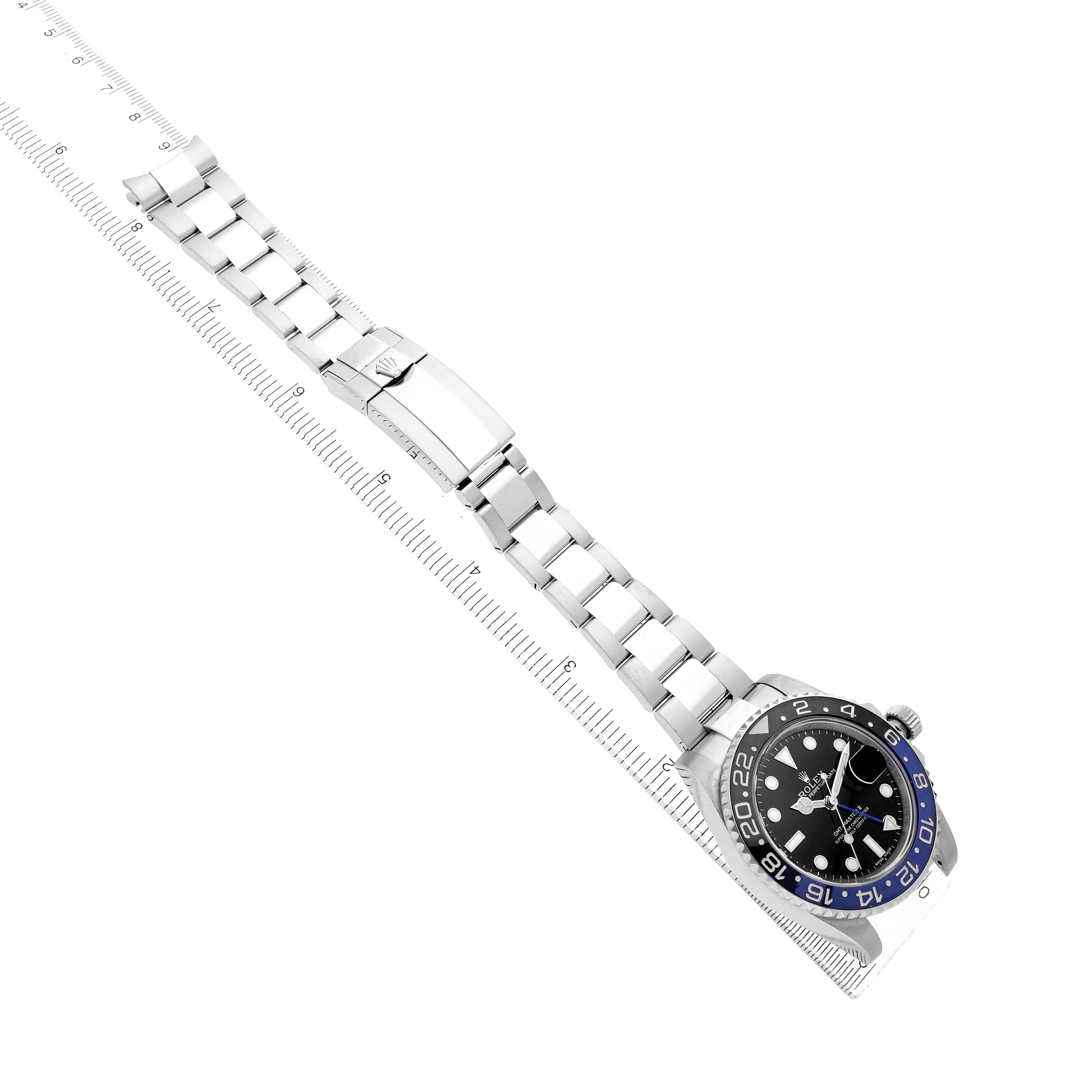 The Rolex GMT-Master 116710 Men's Stainless Steel Black Dial watch is shown at an angle displaying the face, bezel, and full bracelet with a clasp, alongside a ruler for scale.