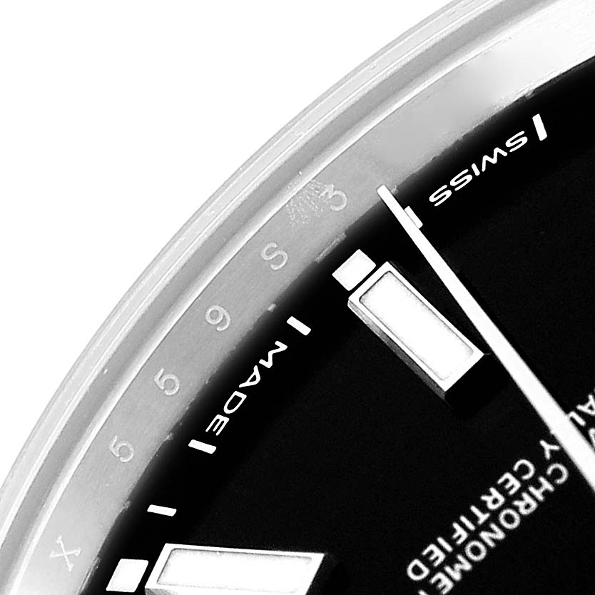 The image shows a close-up of the Rolex Oyster Perpetual 114300 Men's Stainless Steel Black Dial watch, highlighting part of its dial and hour markers.