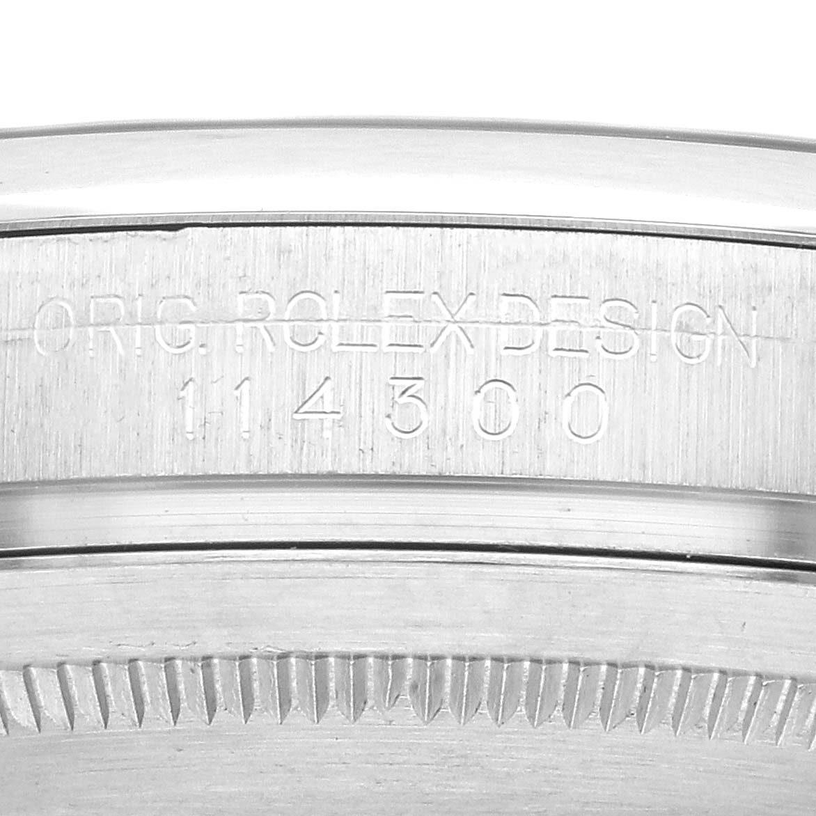 The image shows a close-up of the engraved case back edge of a Rolex Oyster Perpetual 114300 Men's Stainless Steel Black Dial watch.