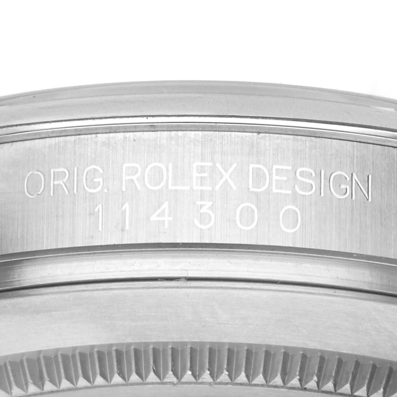 The image shows a close-up of the engraving on the side of a Rolex Oyster Perpetual 114300 Men's Stainless Steel Silver Dial watch case with its model number.