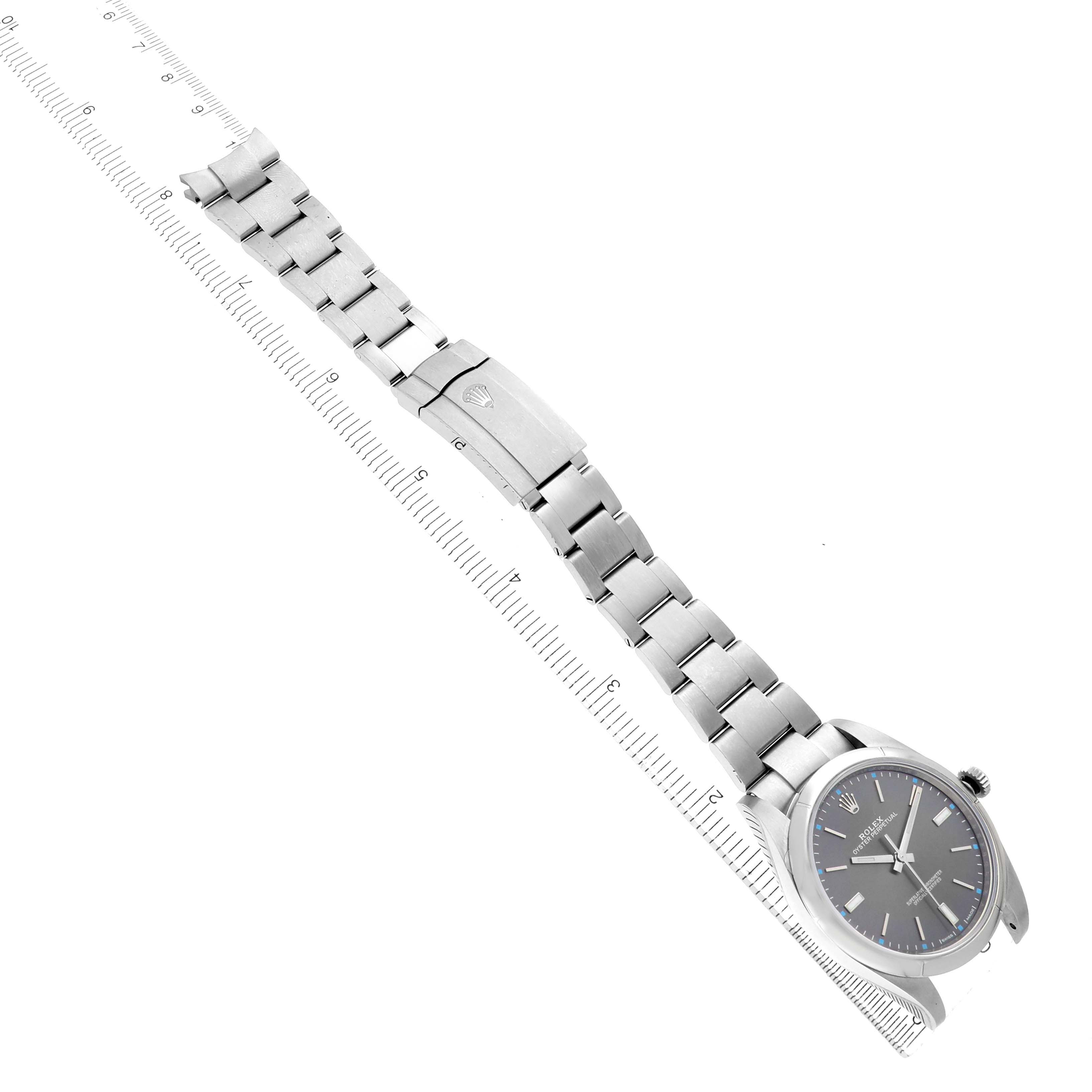 The image shows a Rolex Oyster Perpetual 114300 Men's Stainless Steel Silver Dial watch at an angle displaying its full bracelet, clasp, and dial alongside a ruler.