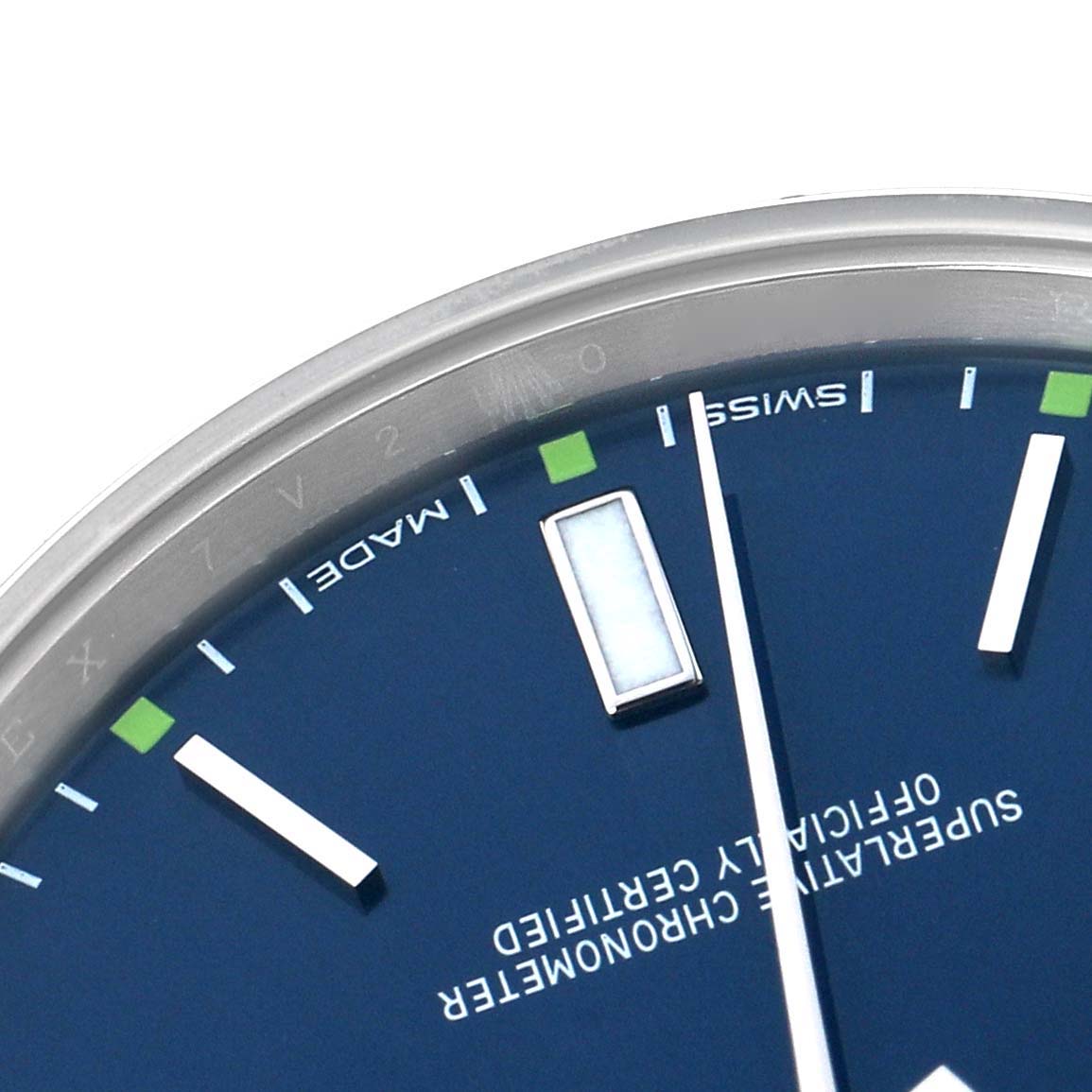 The image shows a close-up of the dial
s upper right corner of the Rolex Oyster Perpetual 114300 Men
s Stainless Steel Blue Dial watch, highlighting the markers and text.
