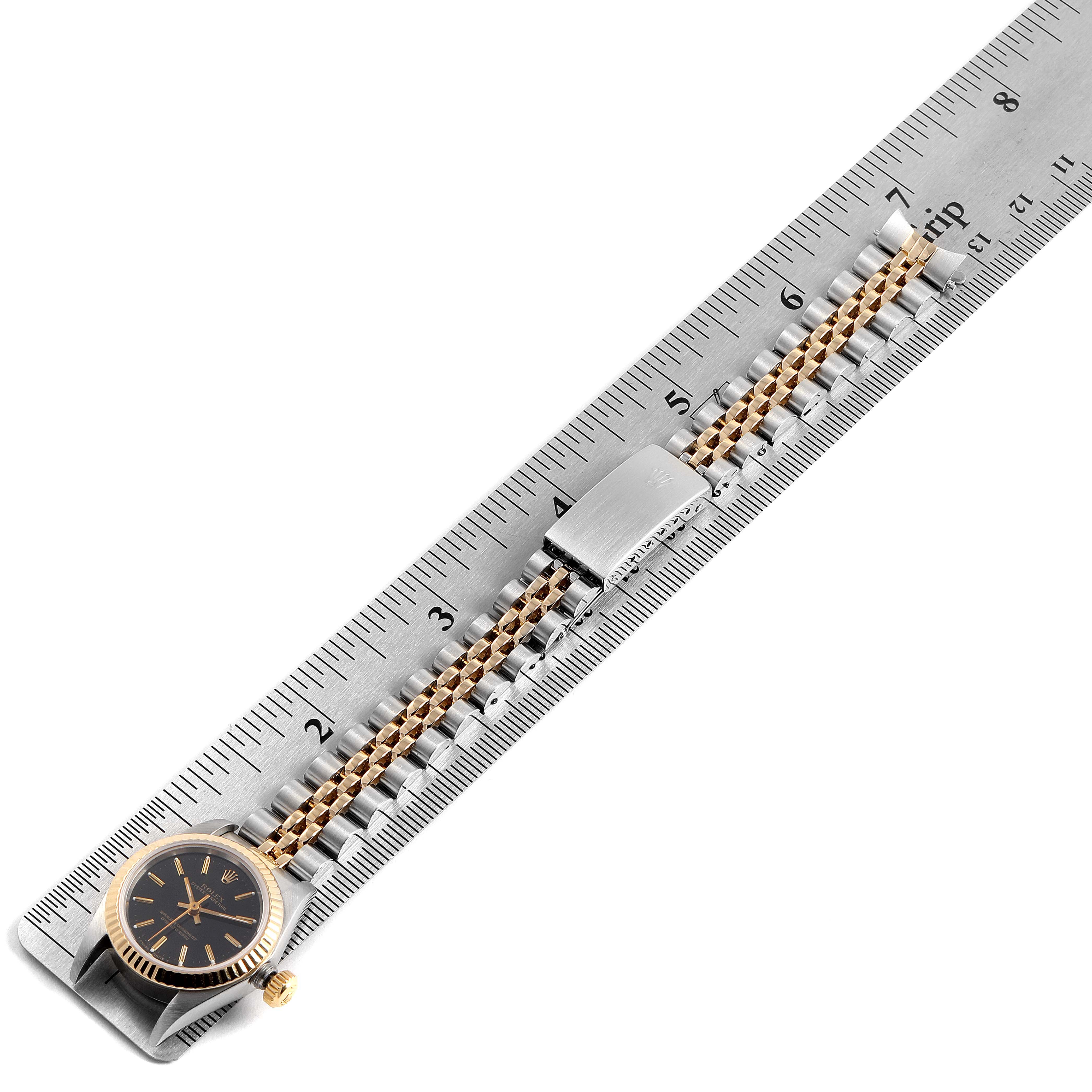 The image shows a Rolex Oyster Perpetual 67193 Women
s Steel and Gold (two tone) Black Dial 67193 Women
s Steel and Gold (two tone) Black Dial watch laid flat with its bracelet and clasp measured against a ruler.