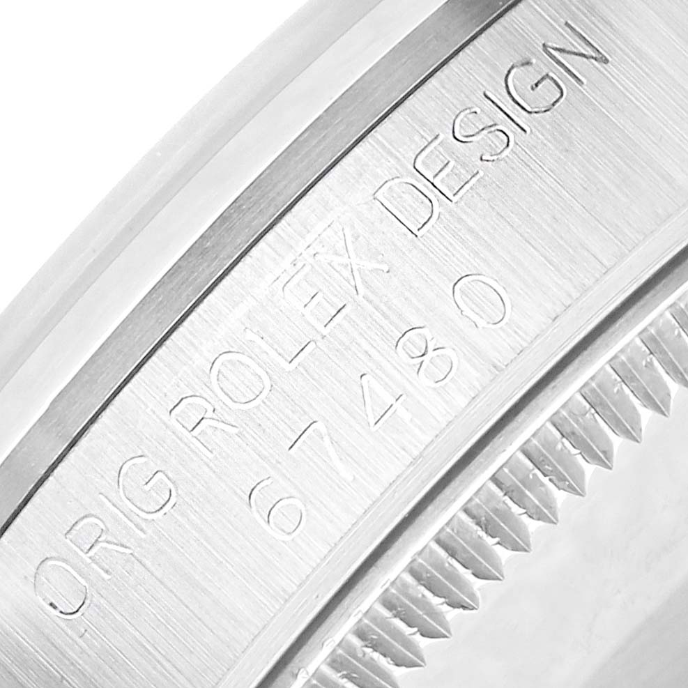 The image shows a close-up of the case back edge of a Rolex Mid-Size 67480 Women
s Stainless Steel Black Dial watch, featuring engraved text and part of the bezel.