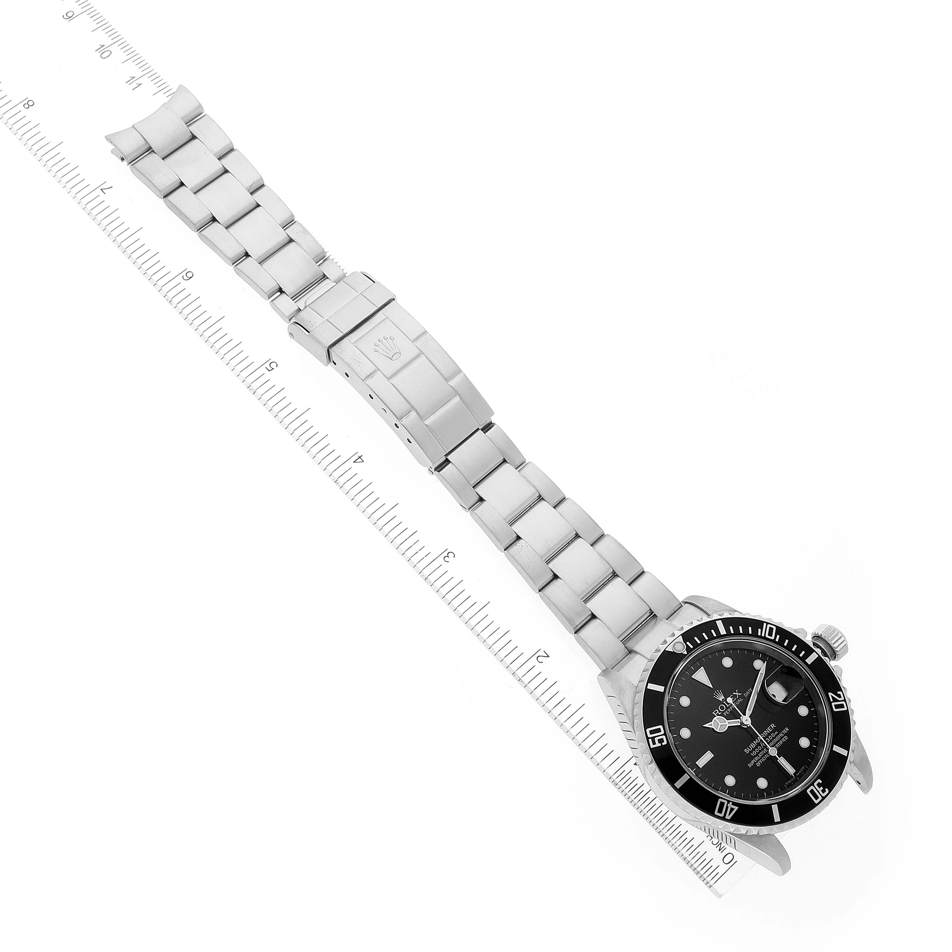 The image shows a Rolex Submariner 16610 Men
s Stainless Steel Black Dial 16610 Men
s Stainless Steel Black Dial watch laid out flat alongside a ruler, displaying the bracelet, clasp, and watch face.