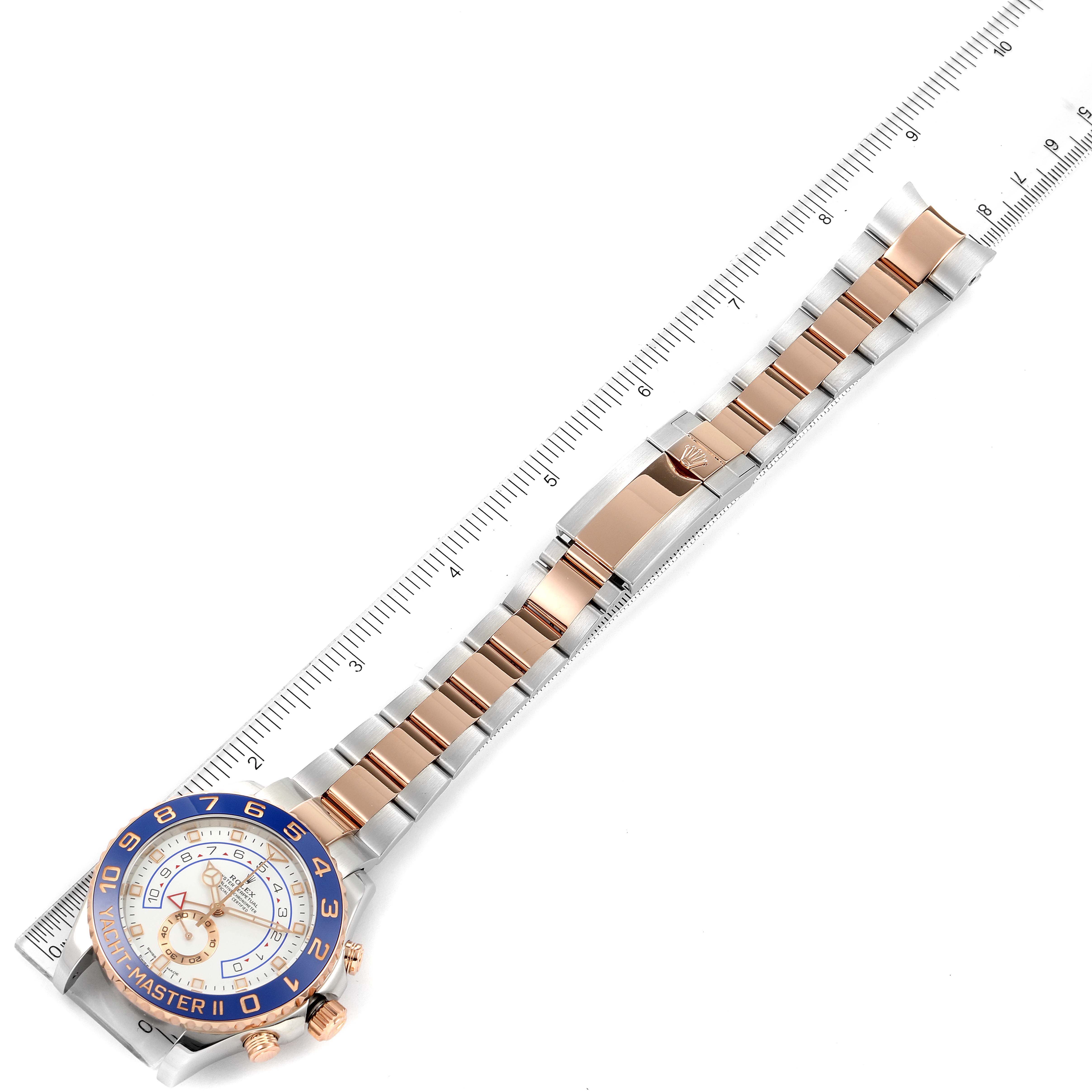 The image shows a bird
s-eye view of a Rolex Yacht-Master 116681 Men
s Steel and Gold (two tone) White Dial 116681 Men
s Steel and Gold (two tone) White Dial watch laid alongside a ruler, displaying its face and bracelet.
