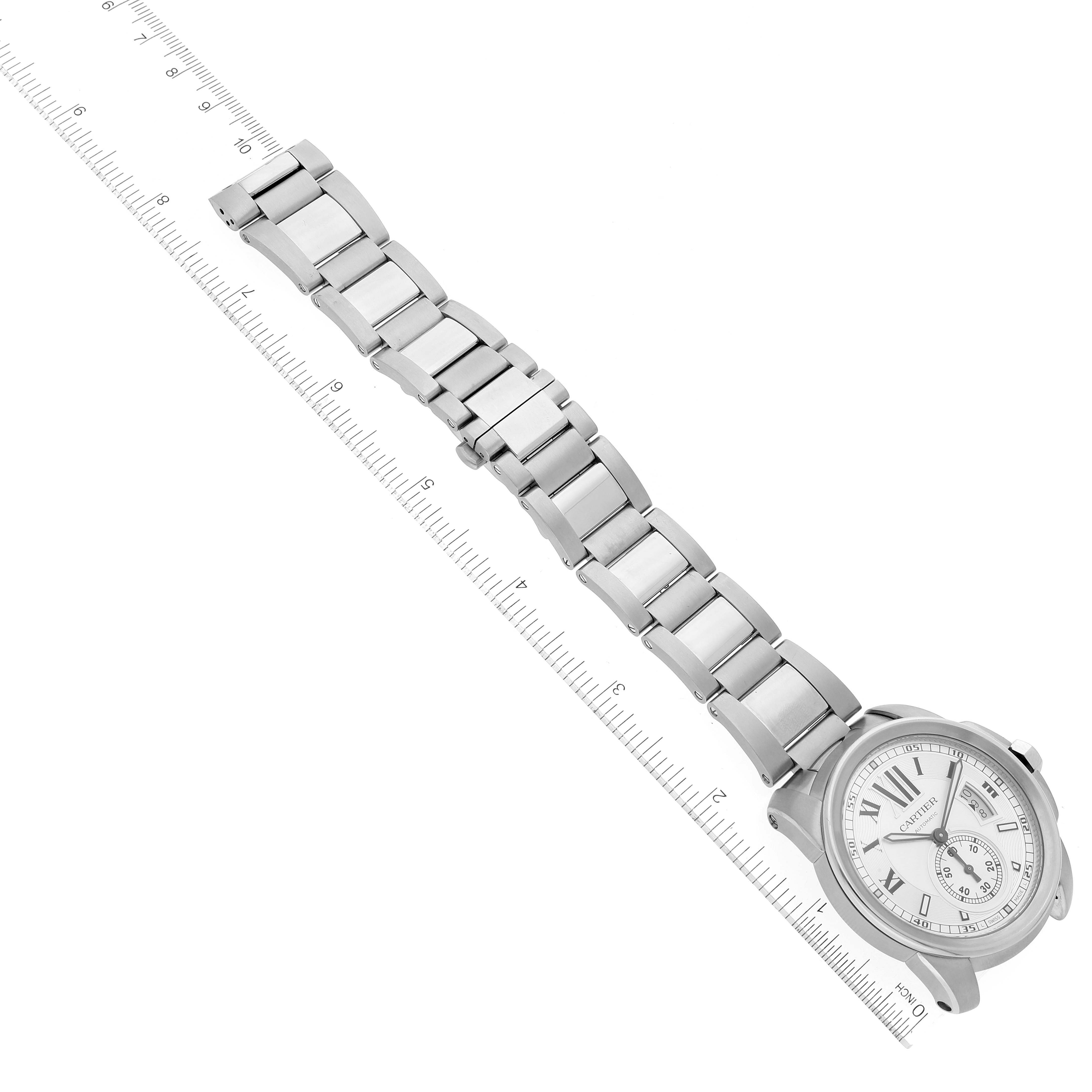 The image shows a Calibre de Cartier watch by Cartier laid flat with its metal bracelet extended alongside a ruler for scale.